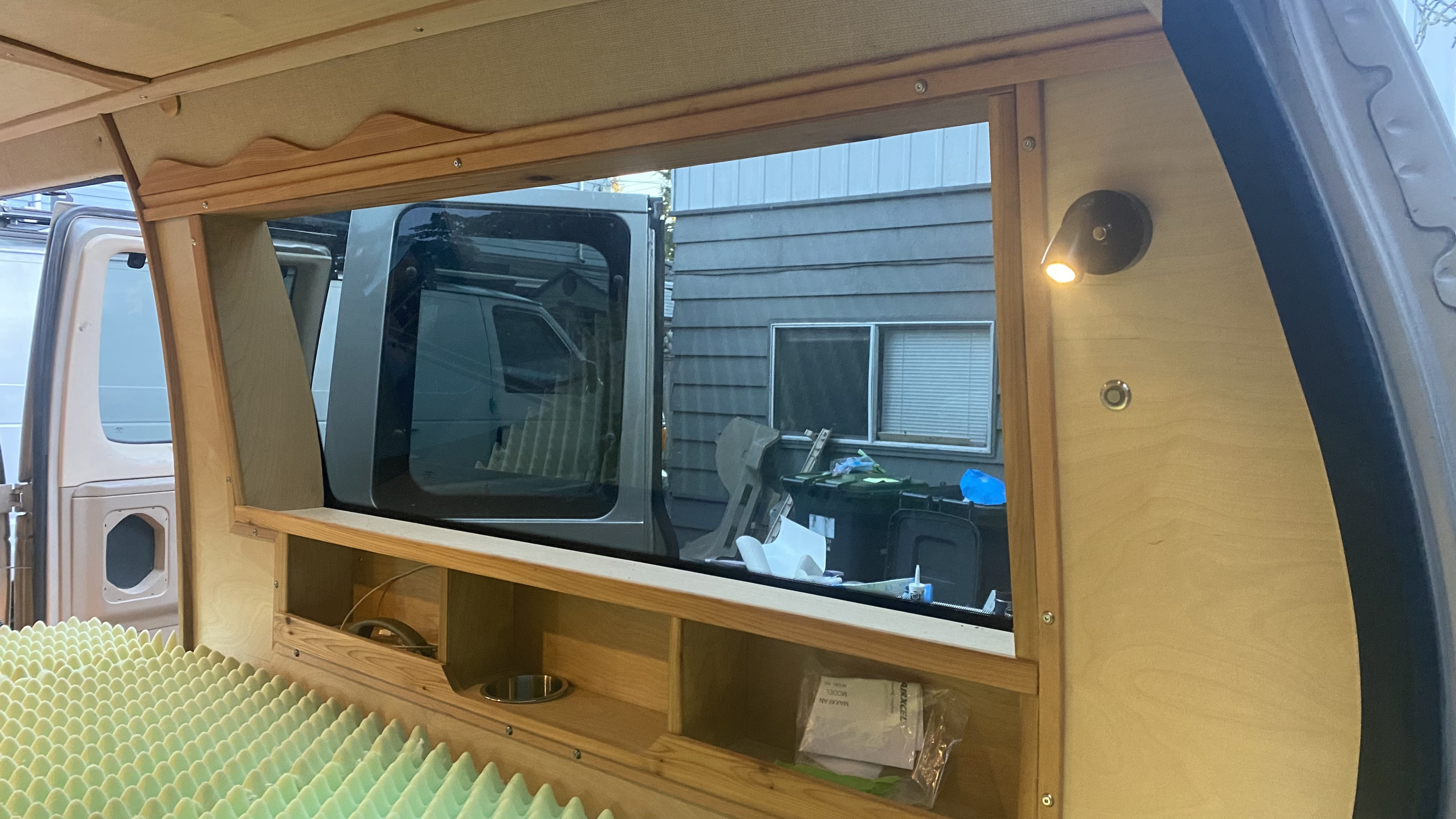 Inside a custom wood rv rental van conversion: bed foam, shelves, and a window view. Ready for your next adventure.. Ford Ford E350 2008