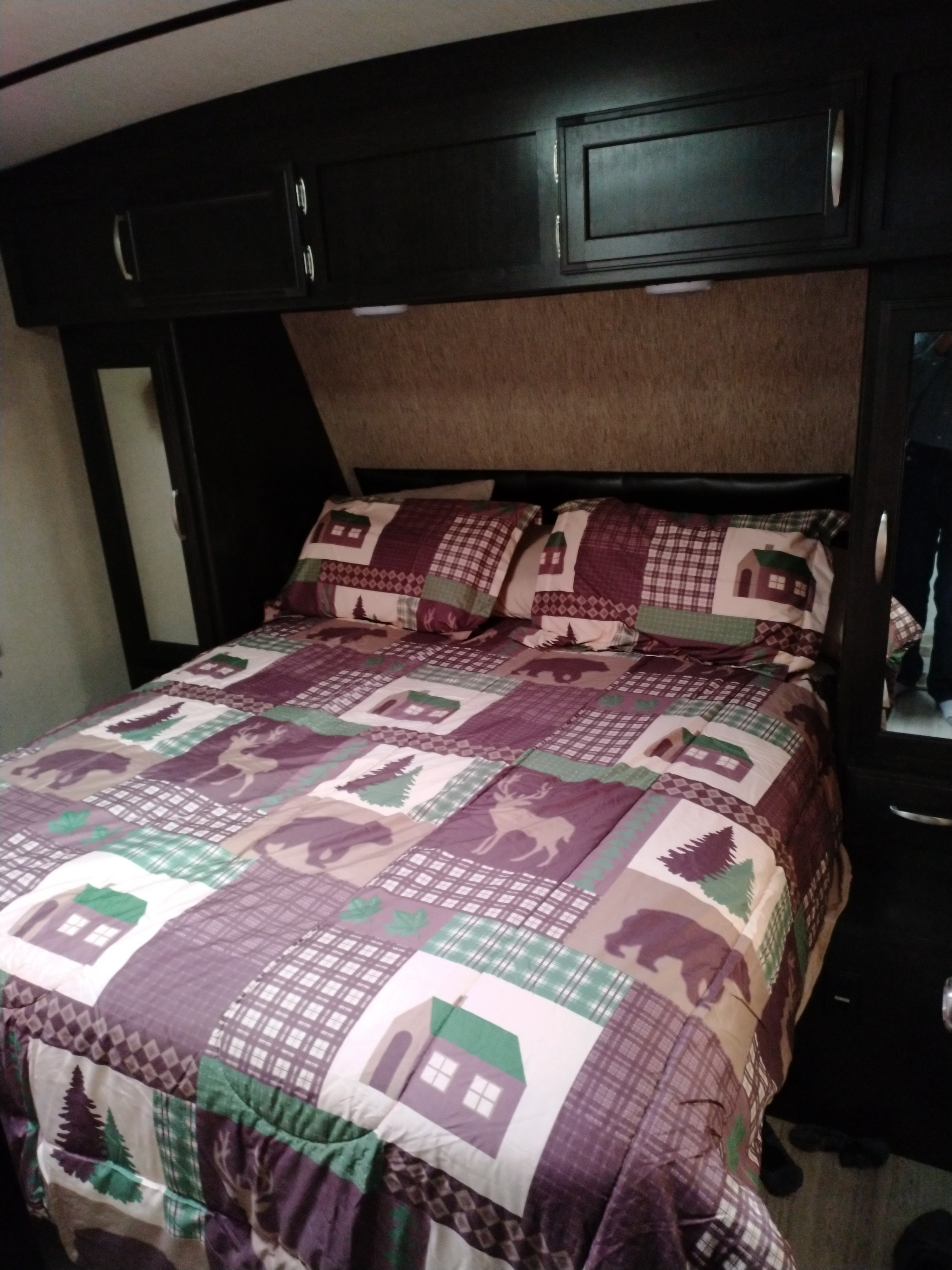 Cozy RV rental bedroom with a rustic-themed comforter, overhead storage, and mirrored wardrobes.. Grand Design Imagine 2017