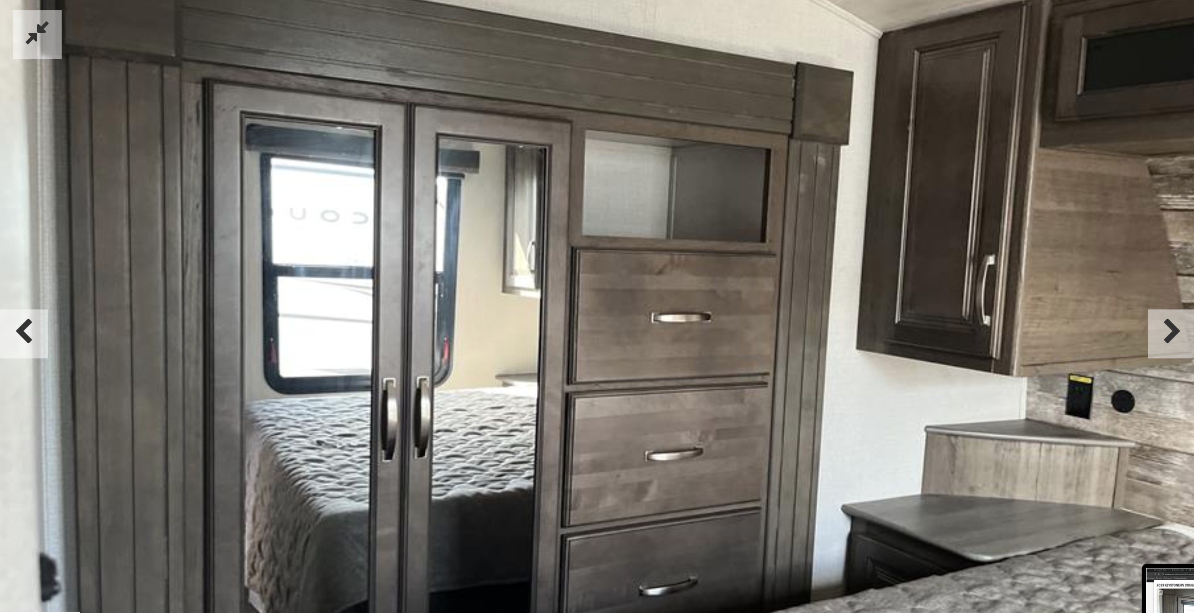 Inside an RV rental bedroom: mirrored wardrobe, dresser with drawers, and a gray quilted bed.. Keystone RV Cougar 2023