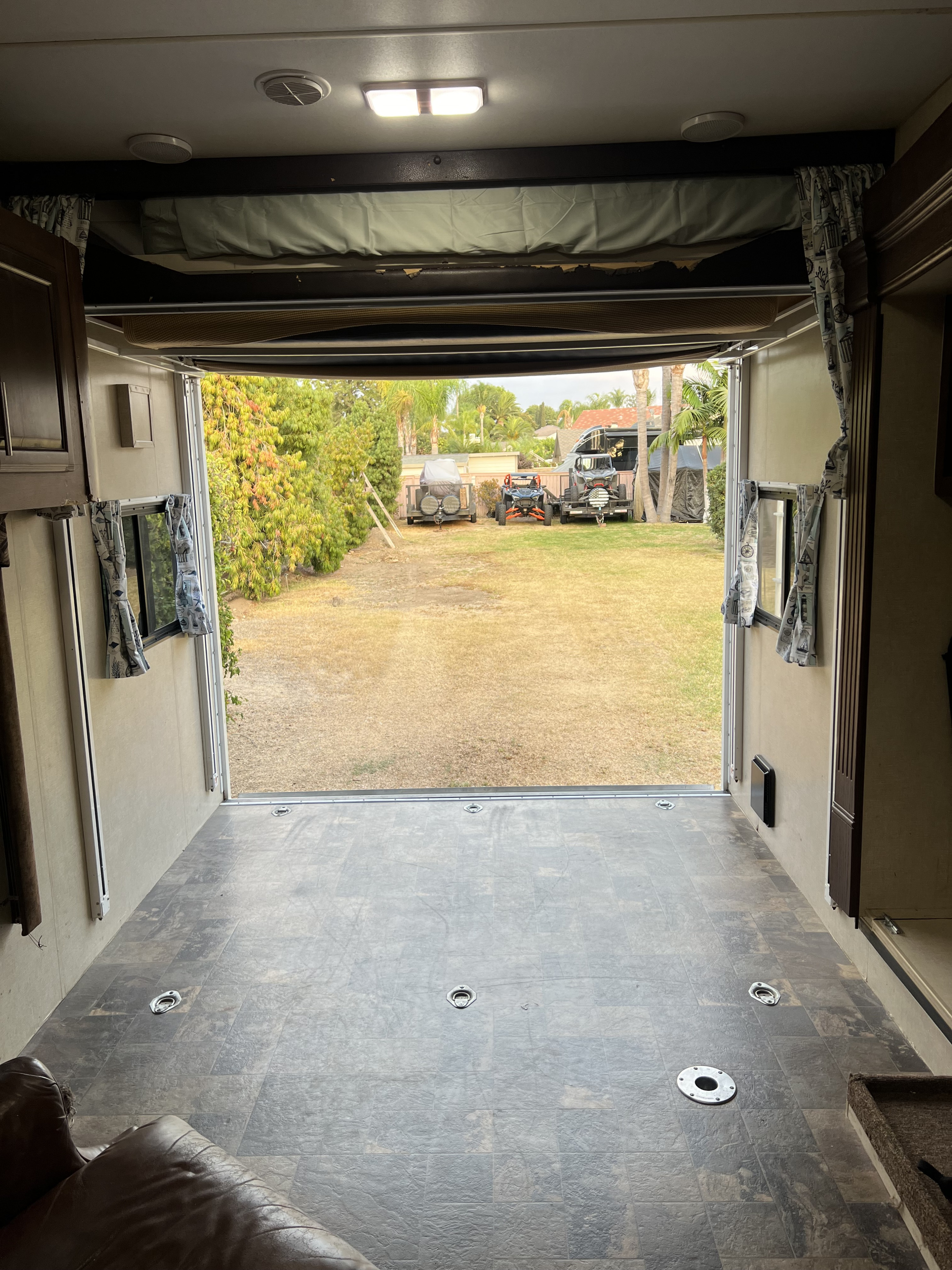 Inside an RV rental toy hauler, its open ramp reveals a backyard with a UTV and other recreational vehicles.. Eclipse Recreational Vehicles Attitude 2014