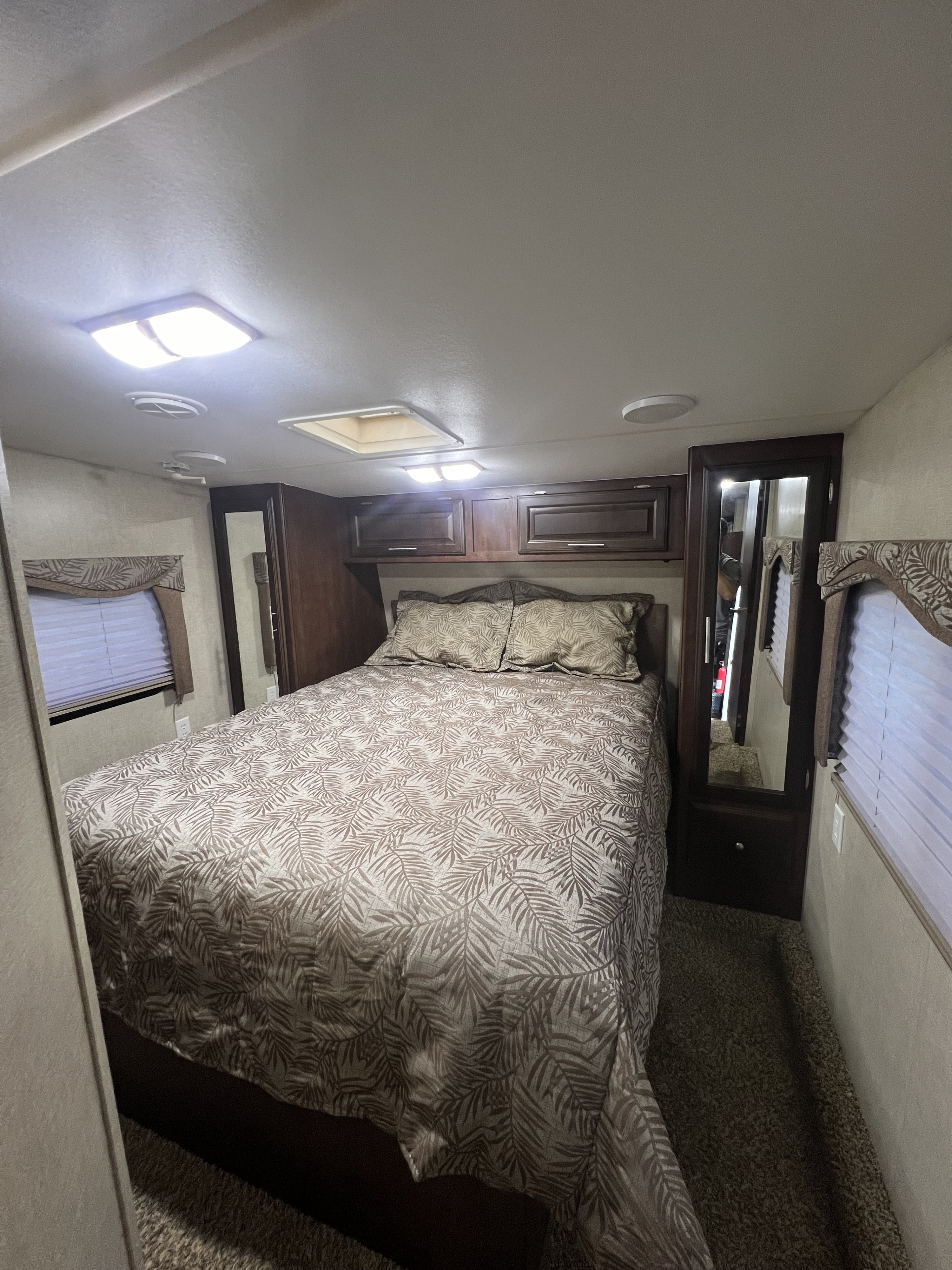 Cozy RV rental bedroom featuring a full bed with a leaf-patterned comforter, overhead cabinets, and windows with blinds.. Eclipse Recreational Vehicles Attitude 2014