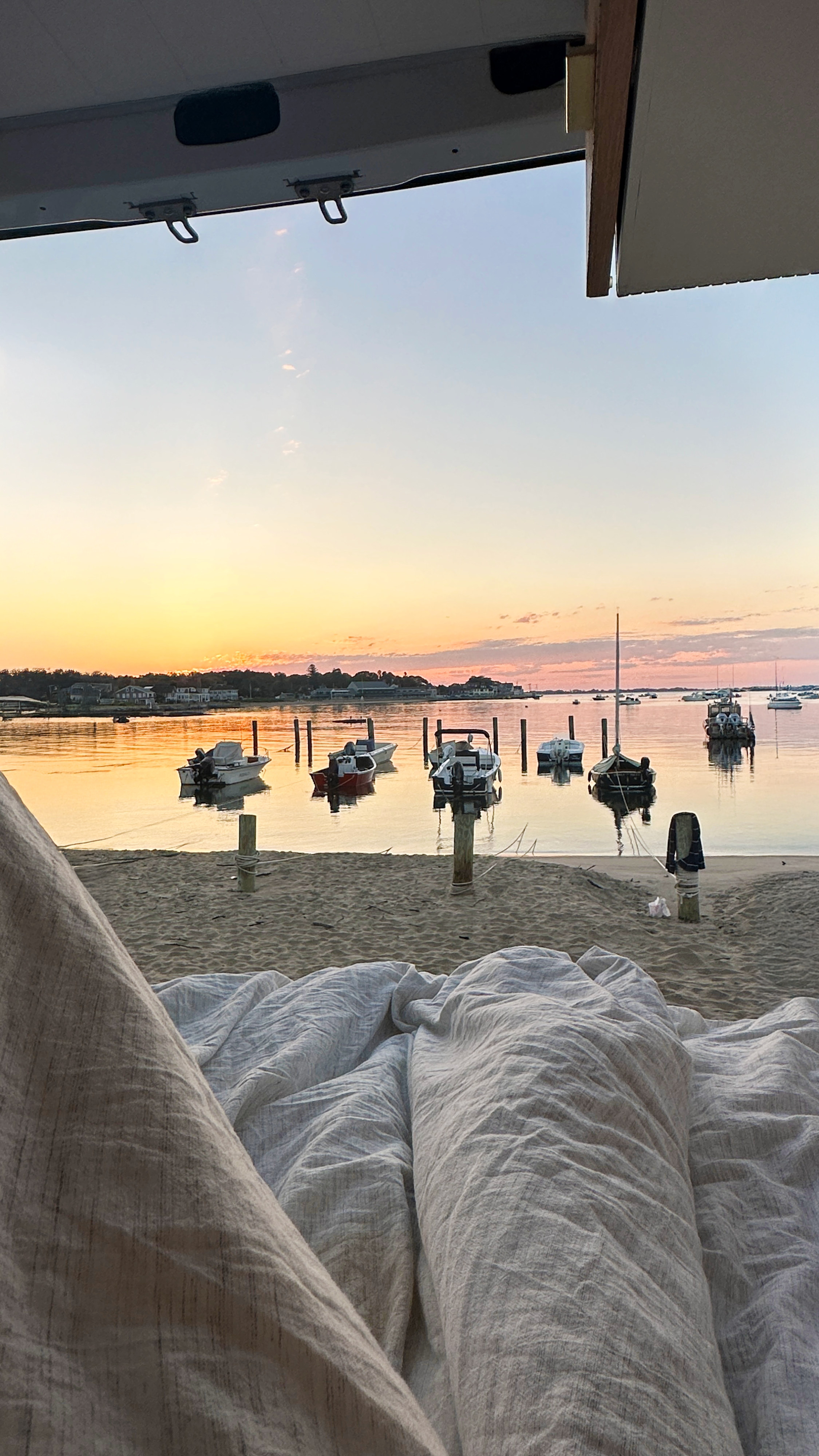 Relaxing inside an RV rental, watching a beautiful sunset over a beach and bay filled with boats. Peaceful van life.. Mercedes-Benz Sprinter 2020