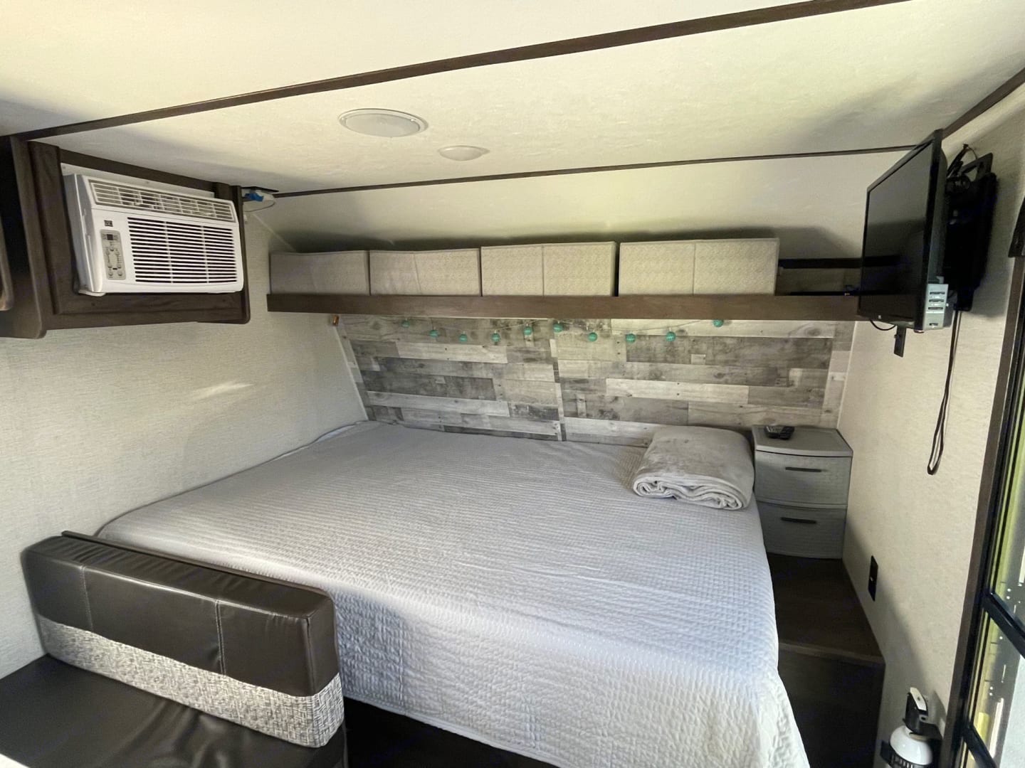 RV rental bedroom: full-size bed, wall-mounted AC, TV, and overhead storage bins create a compact living space.. Dutchmen Coleman Lantern 2021