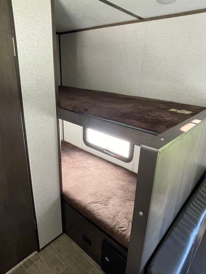 RV rental with cozy bunk beds for family travel. Features two brown plush mattresses, with a window on the lower bed.. Dutchmen Coleman Lantern 2021