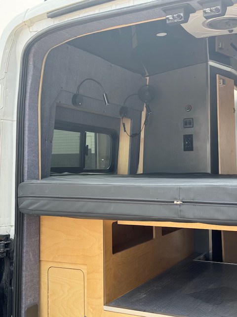 RV rental interior: cozy bed, under-bed storage, and electrical outlets/lights. Ideal for camper van adventures.. Ford Transit 2021