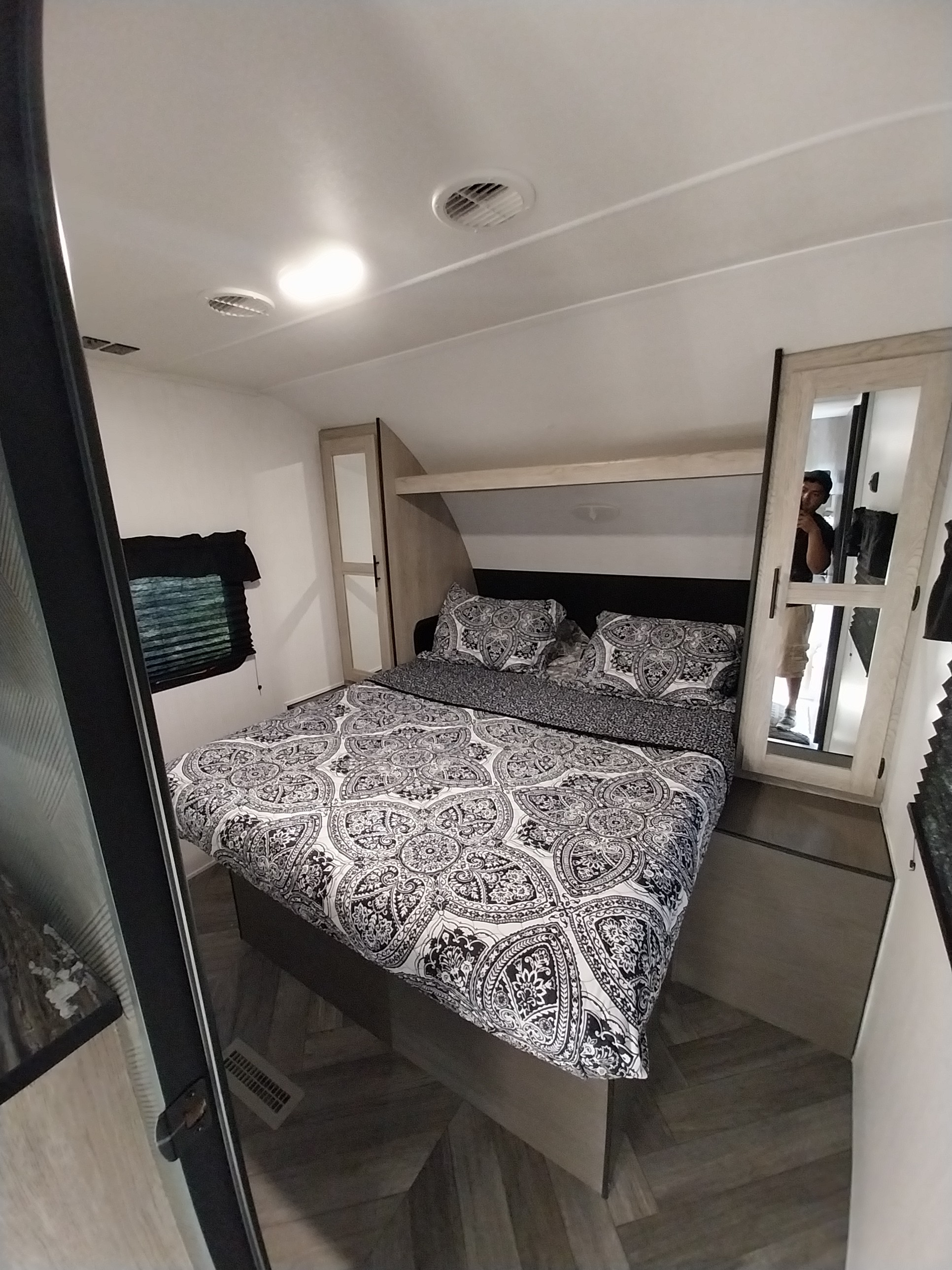 Cozy RV rental bedroom featuring a black and white patterned bed, compact storage, and wood-look flooring.. Heartland RVs Prowler 2023