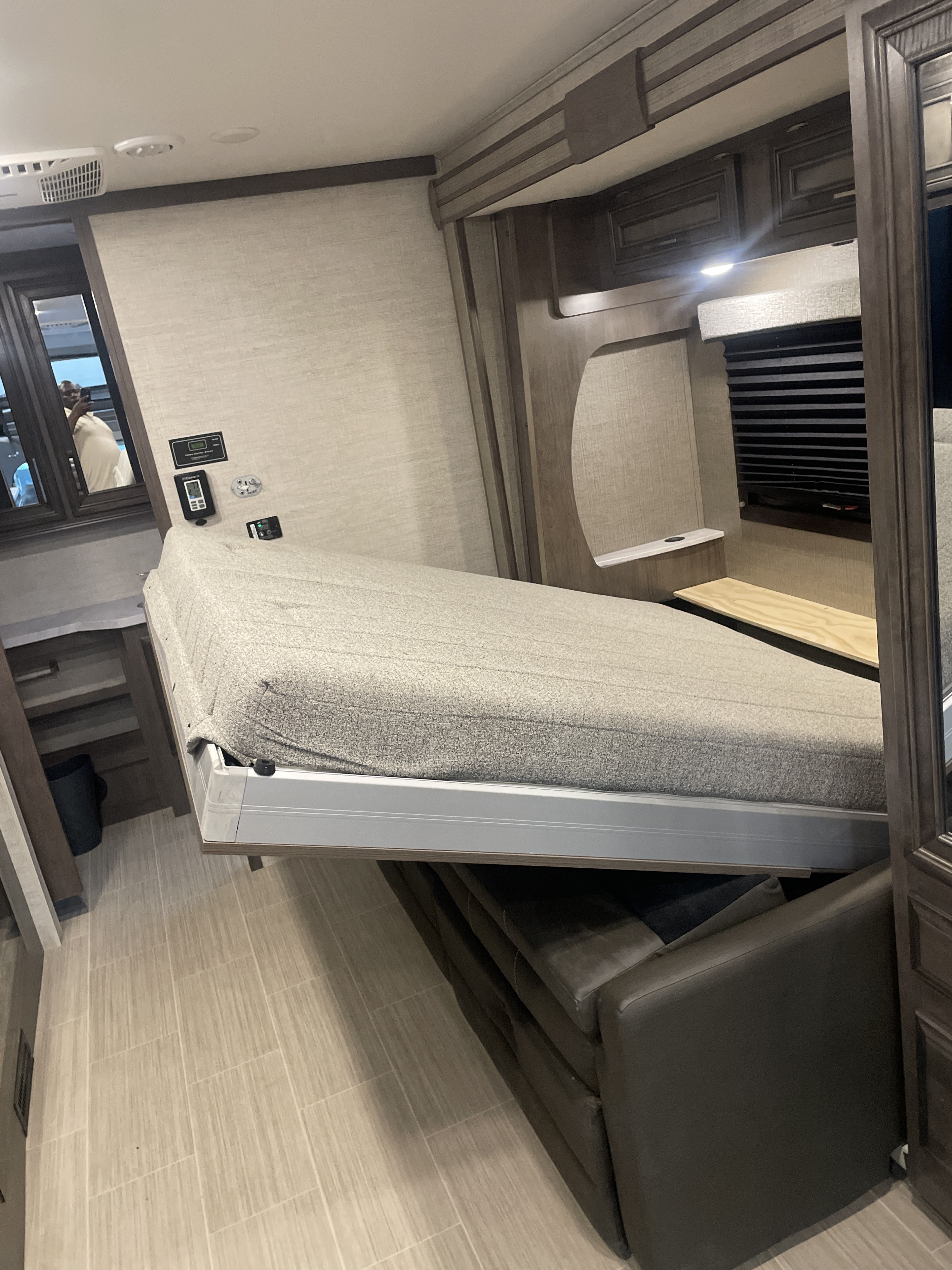 An RV rental interior reveals a fold-down bed extending over a dark sofa, showcasing space-saving design with light tile flooring.. Entegra Coach Other 2022