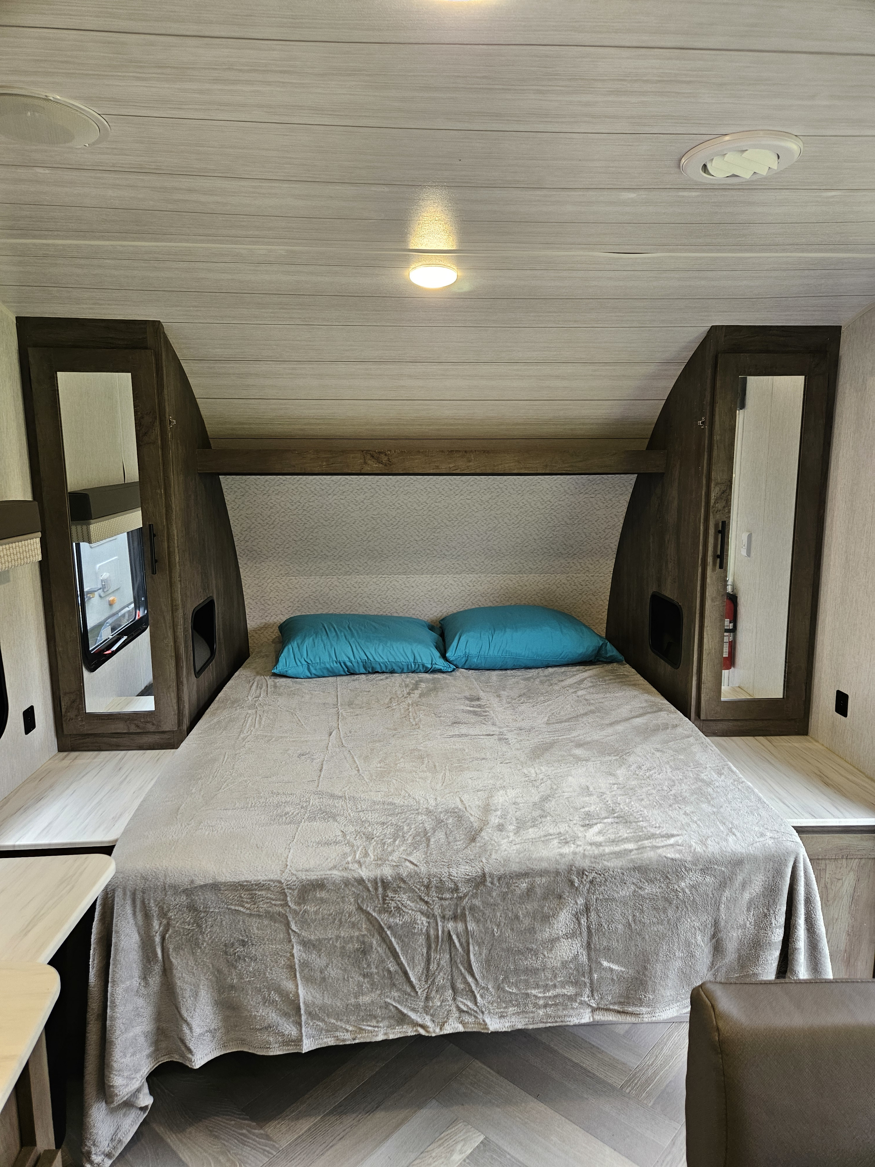 Comfortable RV rental bedroom featuring a queen bed with teal pillows, mirrored cabinets, and modern finishes.. Forest River Wildwood X-Lite 2021