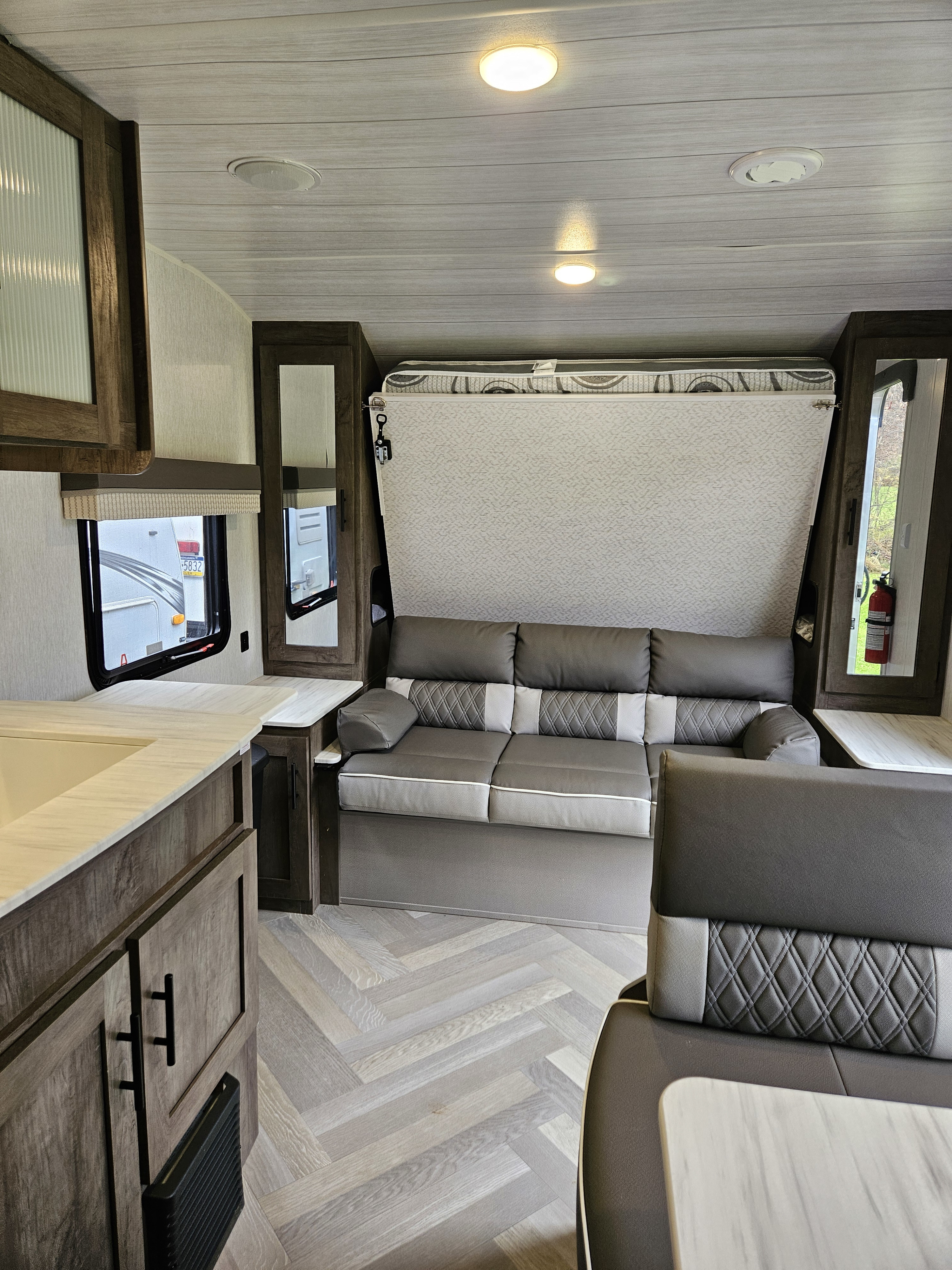 Modern rv rental interior with a folding bed over a sofa, compact kitchen area, and stylish herringbone flooring.. Forest River Wildwood X-Lite 2021