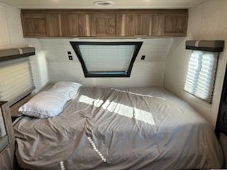 This RV rental's bedroom offers a large bed with light bedding, overhead wood cabinets, and windows with blinds for comfortable travel.. Palomino Palomini 2022