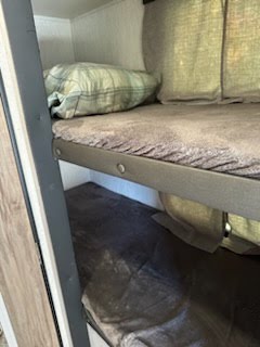 An RV rental interior shows two metal-framed bunk beds. The top bunk has pillows, the bottom a dark blanket, ready for sleeping.. Palomino Palomini 2022