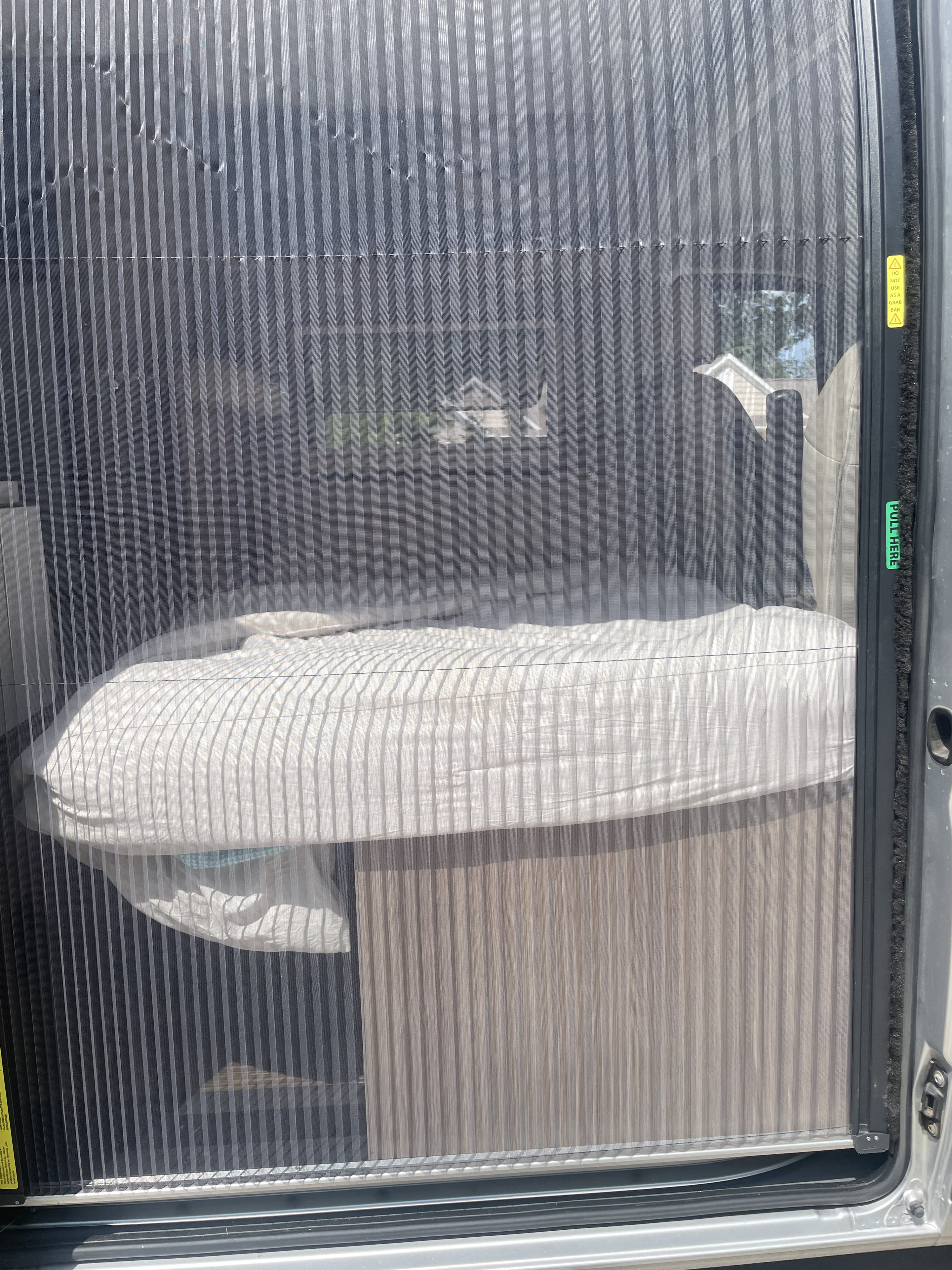 RV rental's pleated screen door showing interior mattress setup & exterior view. Warning: Do not use as grab bar.. Winnebago Travato 2019
