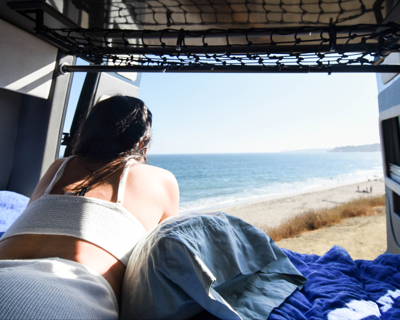 A person relaxes in an RV rental, enjoying sunny ocean and beach views from inside the camper van.. Airstream Interstate 2015