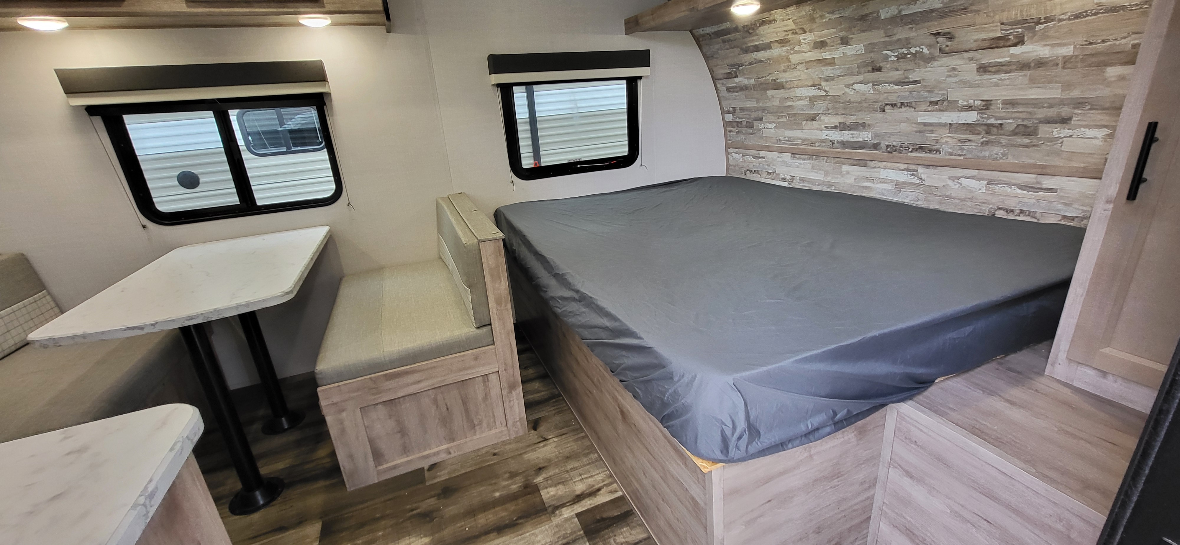 RV rental interior: modern dinette with table and benches, and a bed with a grey cover. Light wood decor throughout.. Gulf Stream Ameri-Lite 2024