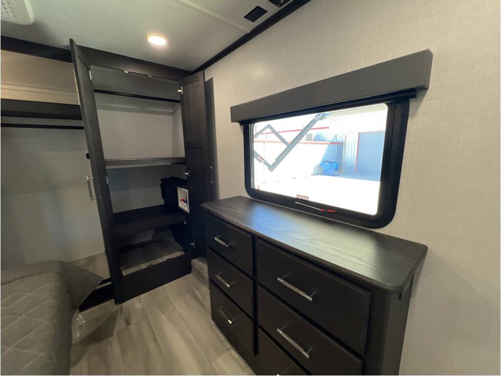 RV rental bedroom: dark wood wardrobe with shelves & washer/dryer hookup. Features a dresser, window, and bed.. Keystone Alpine 2025