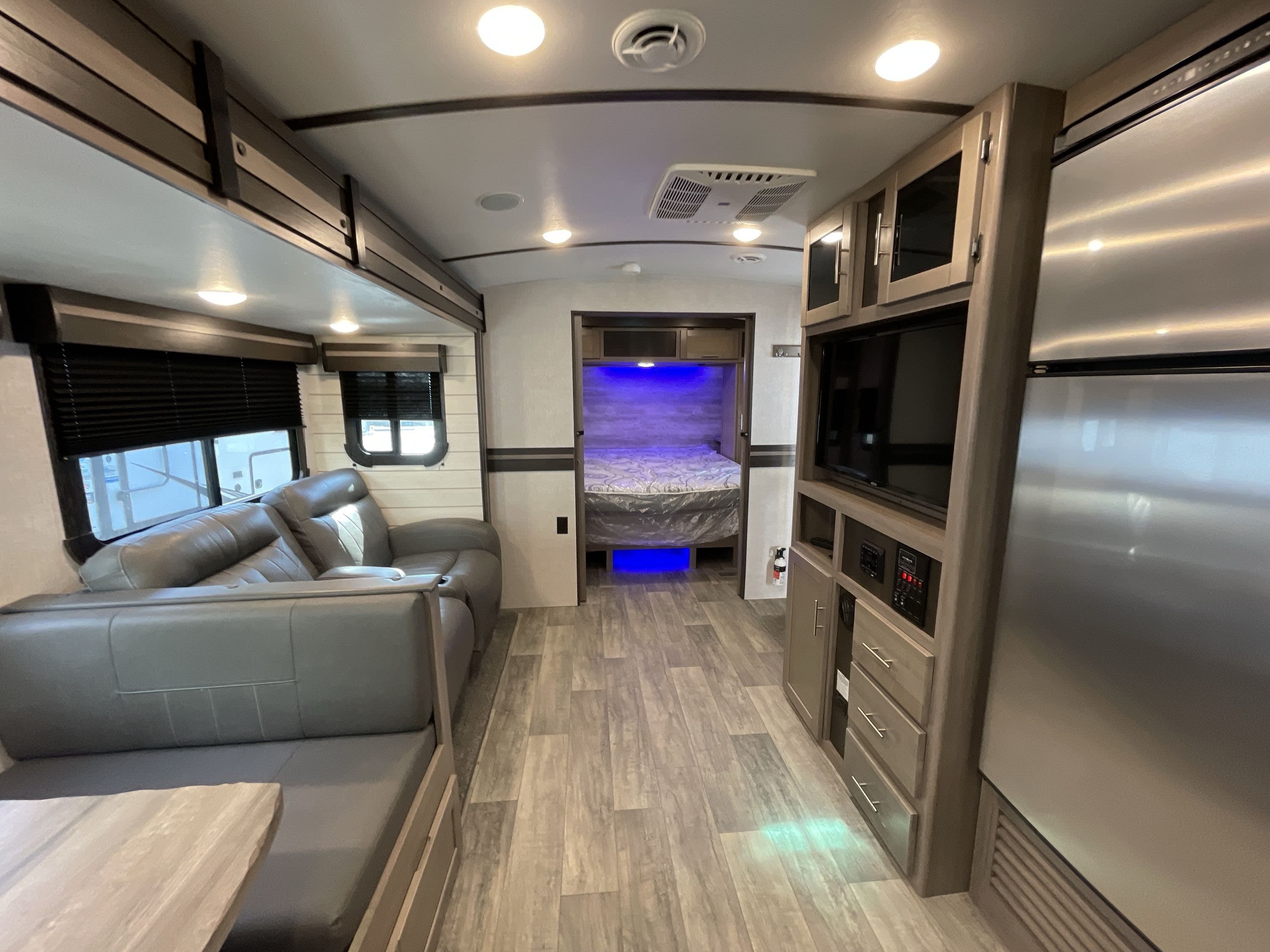 Inside a spacious RV rental, showing a modern living area, entertainment center, fridge, and a cozy bedroom with blue lights.. Crossroads Sunset Trail Super Lite 2021