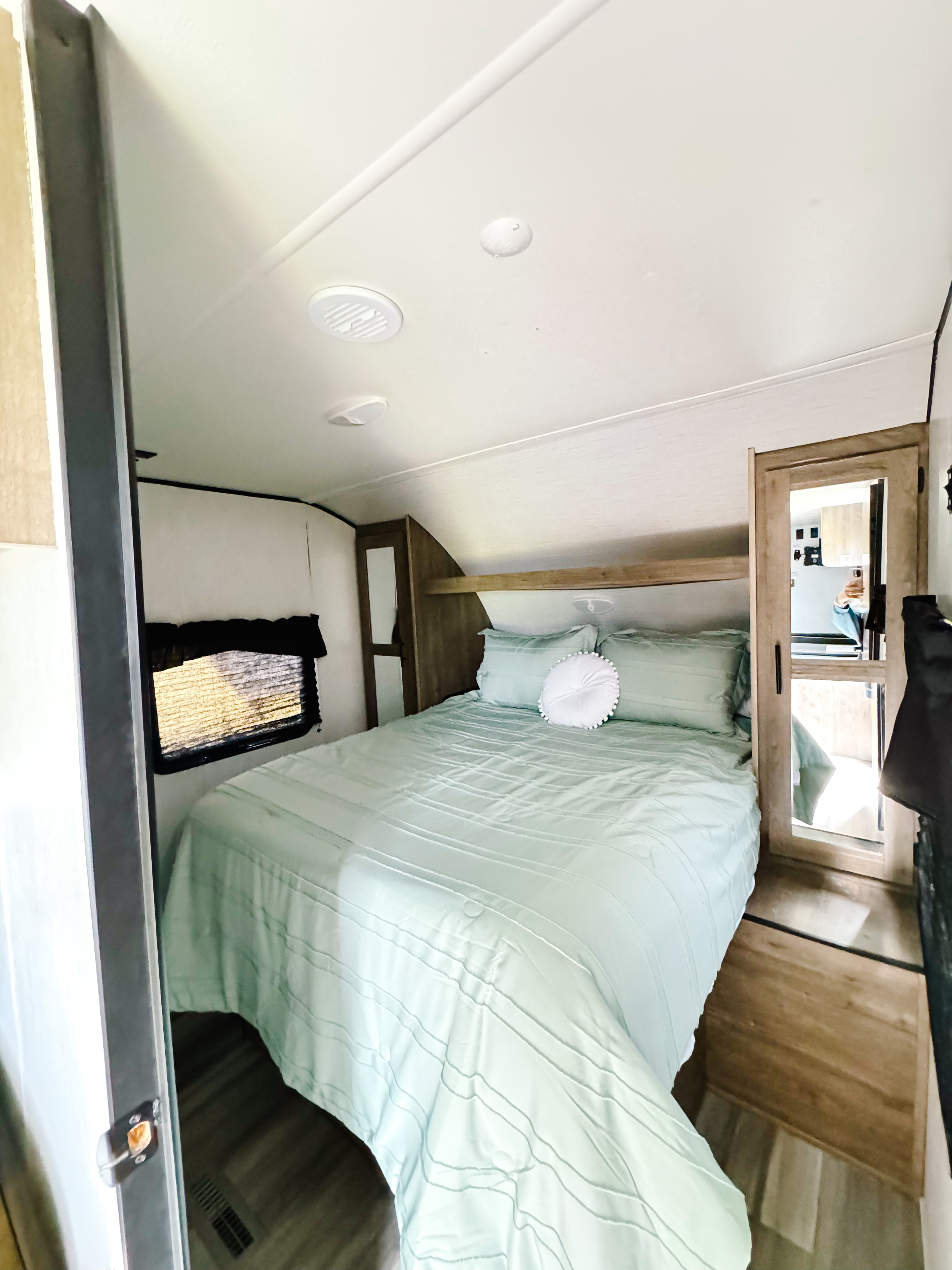 Bright RV rental bedroom showcasing a bed with fresh mint green bedding, a window, and wood storage. Ready for travel!. Heartland RVs Pioneer 2022