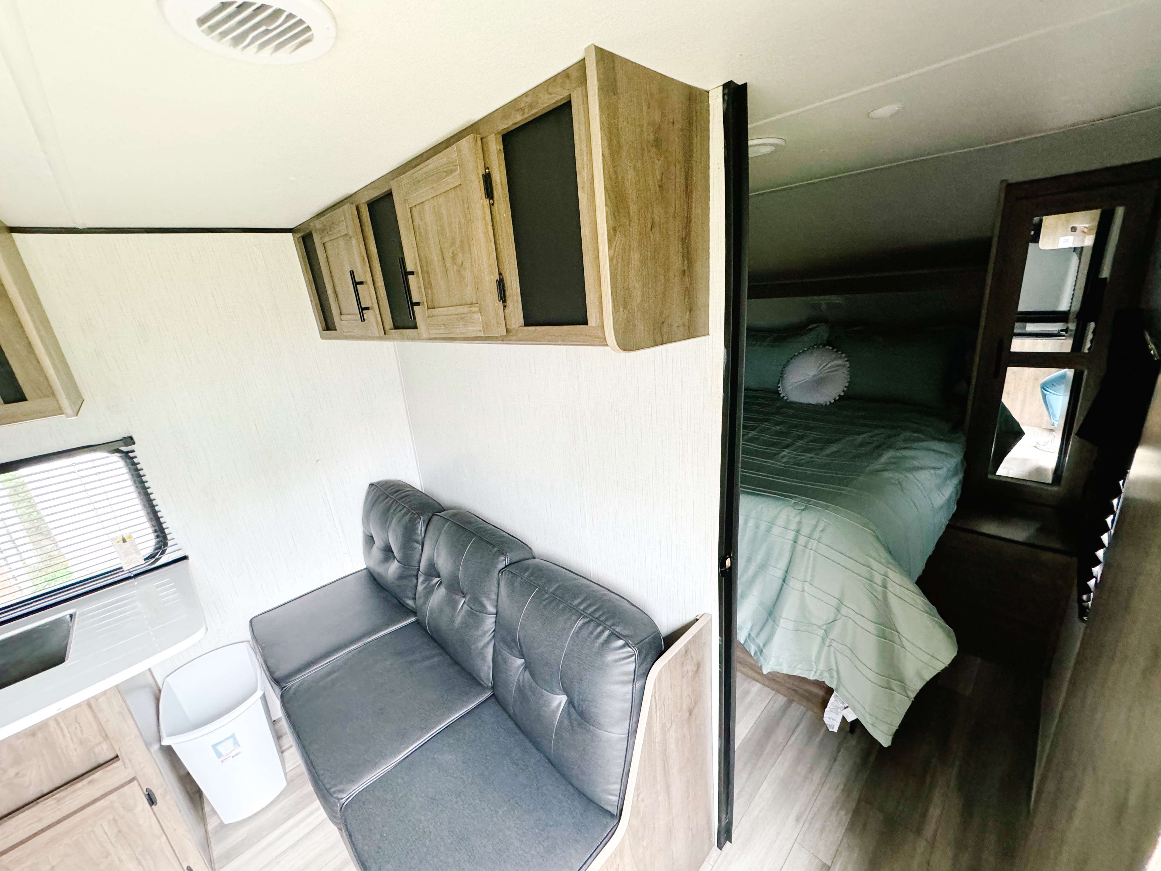 This RV rental interior showcases a living area with a dark sofa and cabinets, peeking into a cozy bedroom with a bed.. Heartland RVs Pioneer 2022