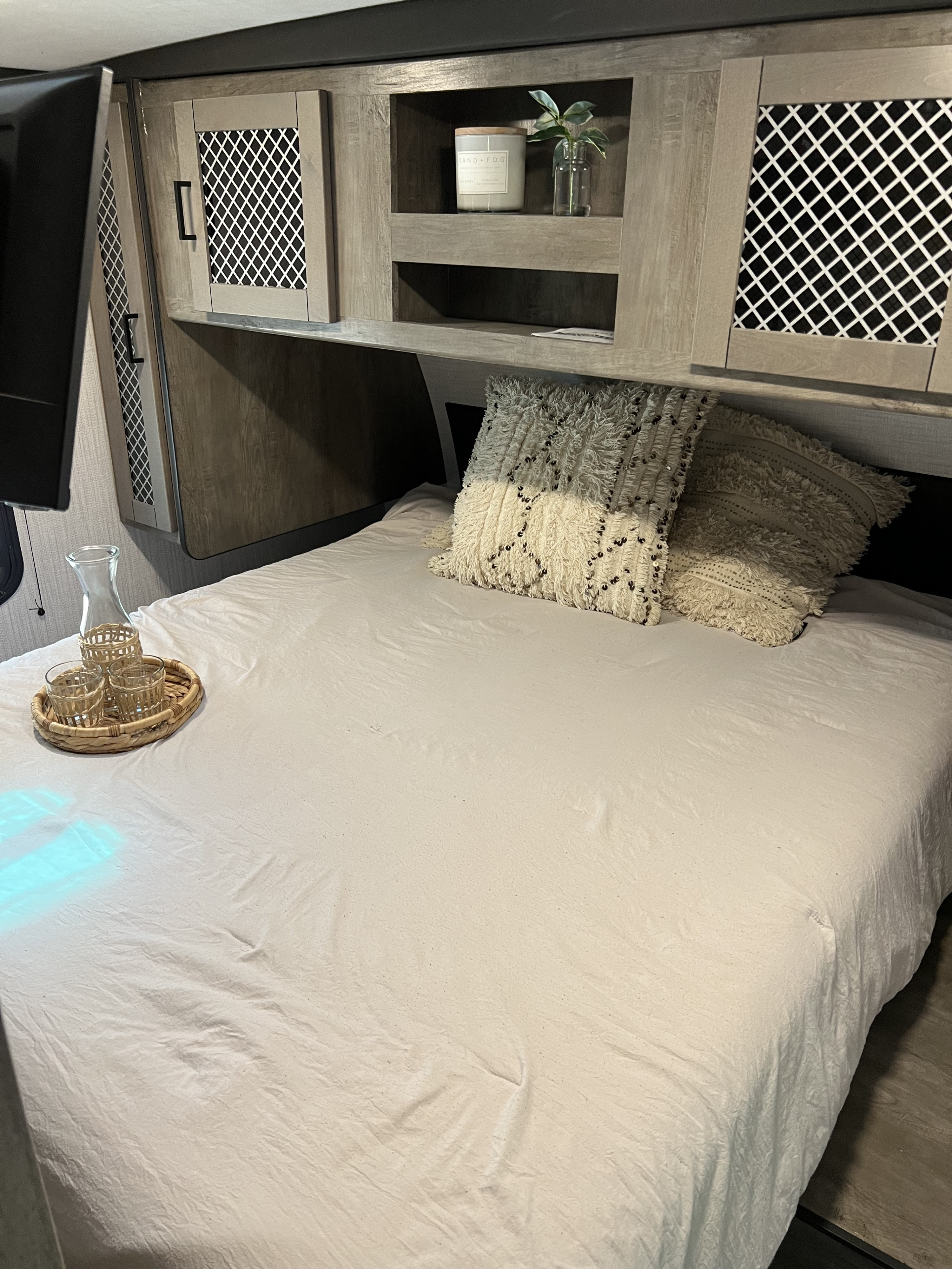 Cozy RV rental bedroom featuring clean white bedding, overhead cabinets with decor, and a convenient TV.. Heartland RVs North Trail 2021