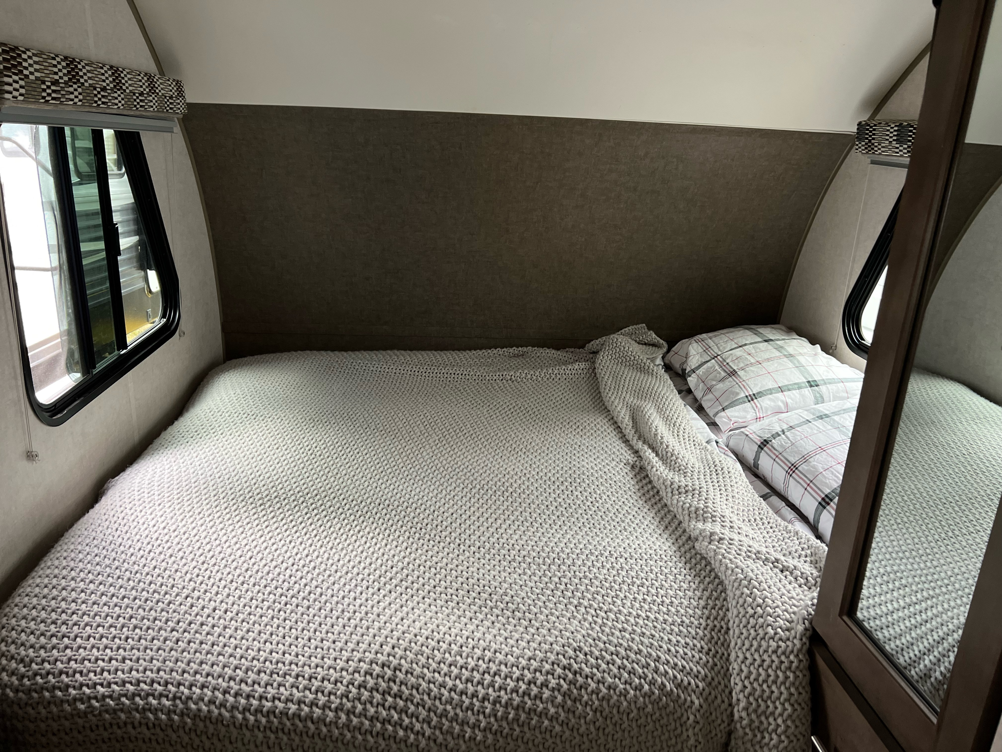 An RV rental's inviting bedroom featuring a comfy bed with grey knitted blanket, plaid pillows, and a window.. Forest River R-Pod 2018