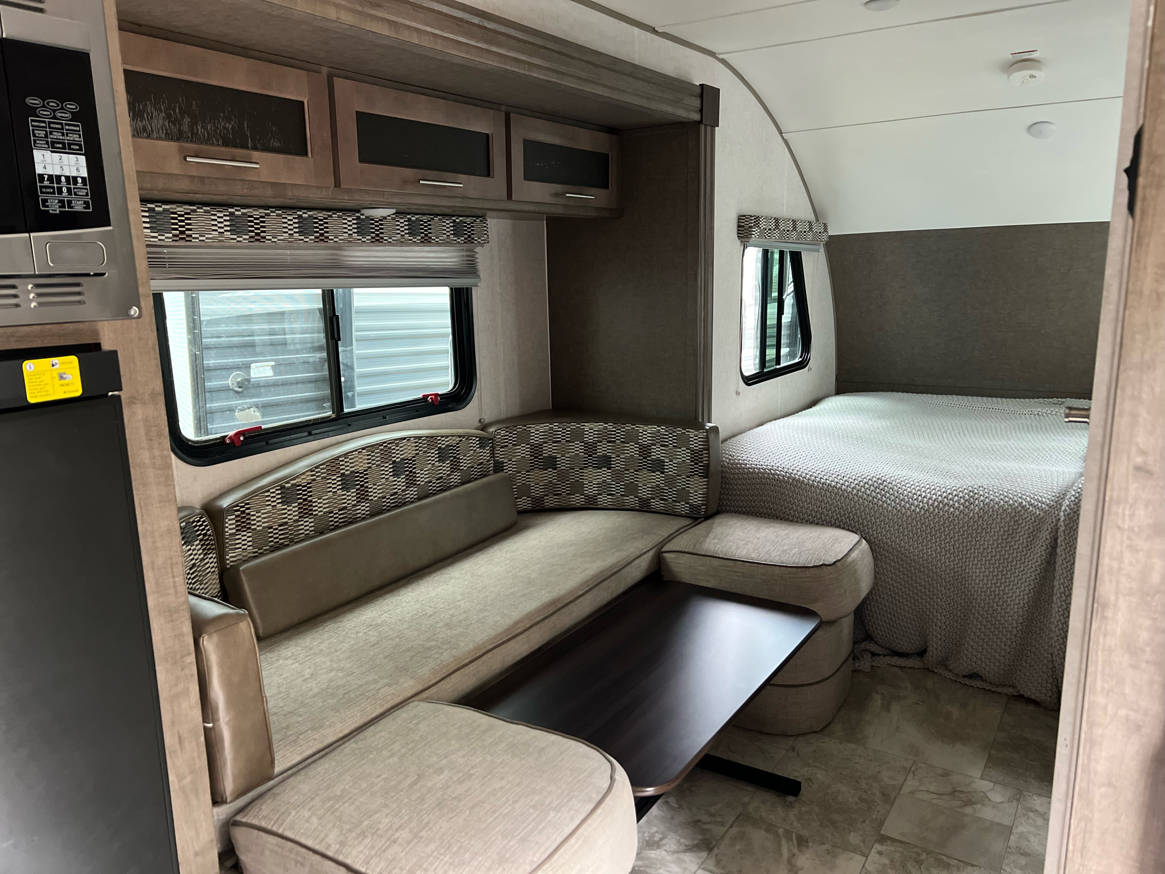 This RV rental shows a practical interior: a lounge with a table, microwave, and bed covered in a textured blanket.. Forest River R-Pod 2018