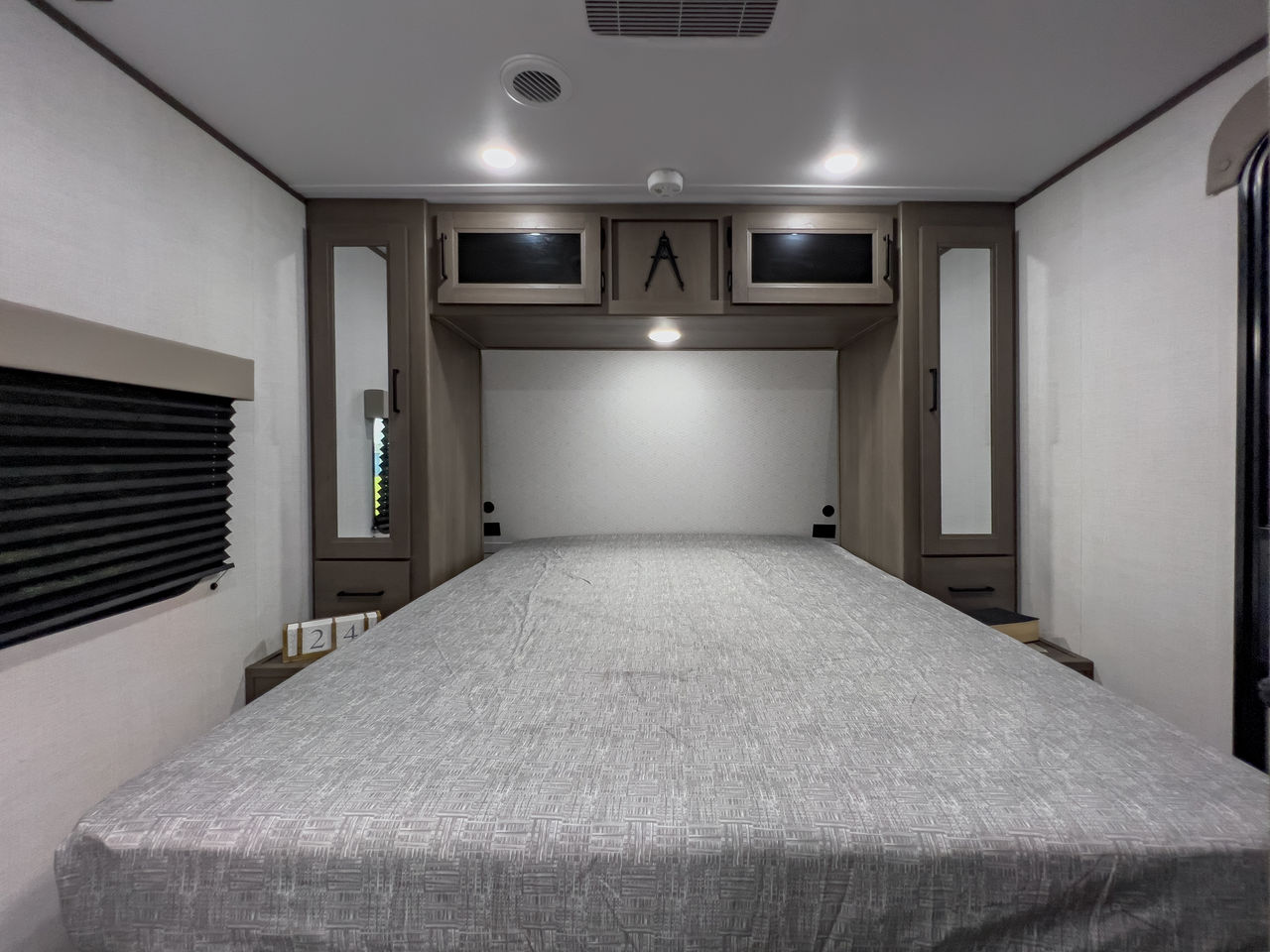 Comfortable RV rental bedroom featuring a large bed, overhead cabinets, and mirrored wardrobes. Ideal for your next trip.. Grand Design Transcend Xplor 2025