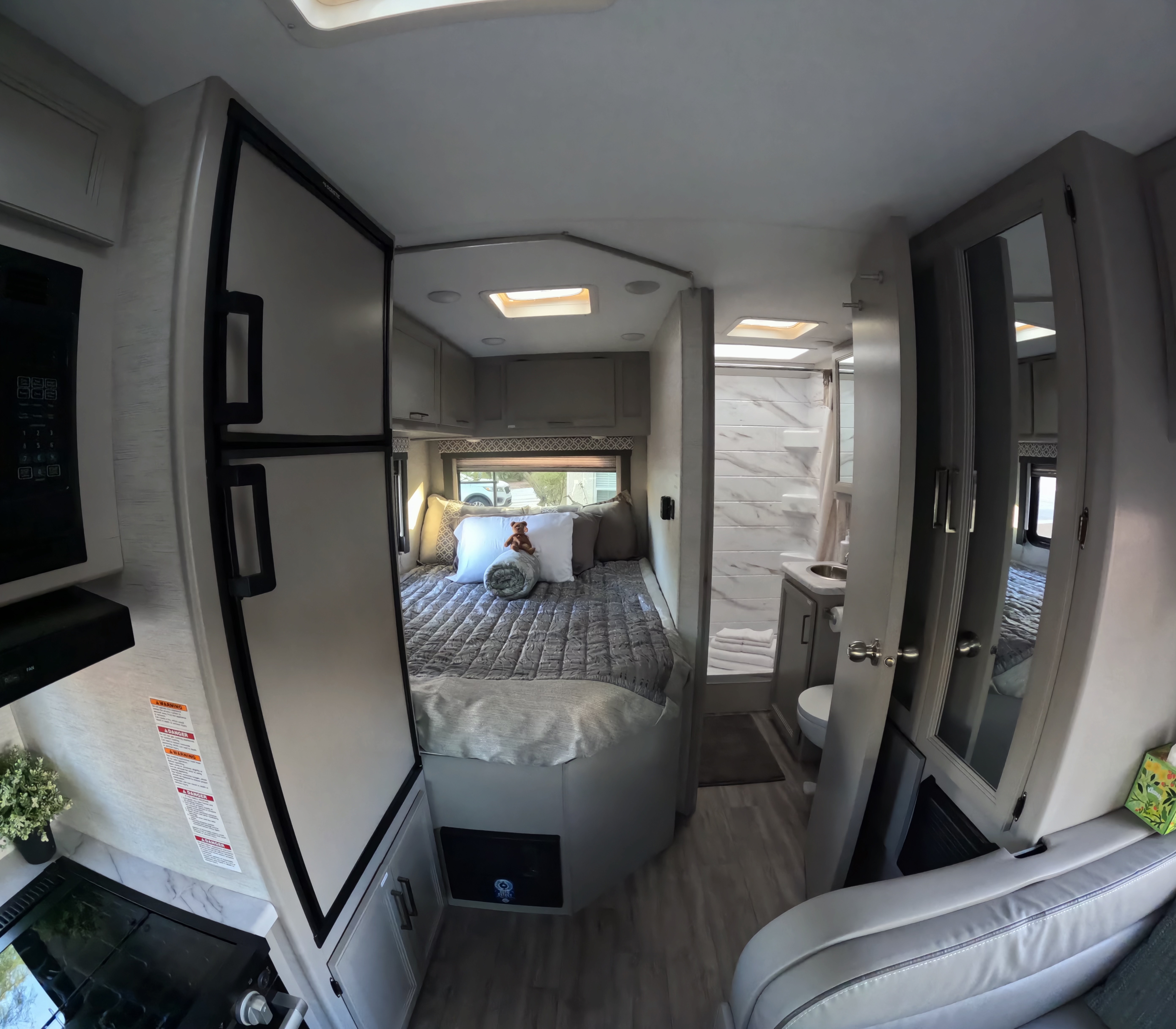 Modern RV rental interior with a cozy bed, compact shower/toilet, and kitchenette, ready for your next adventure.. Thor Coleman 2024