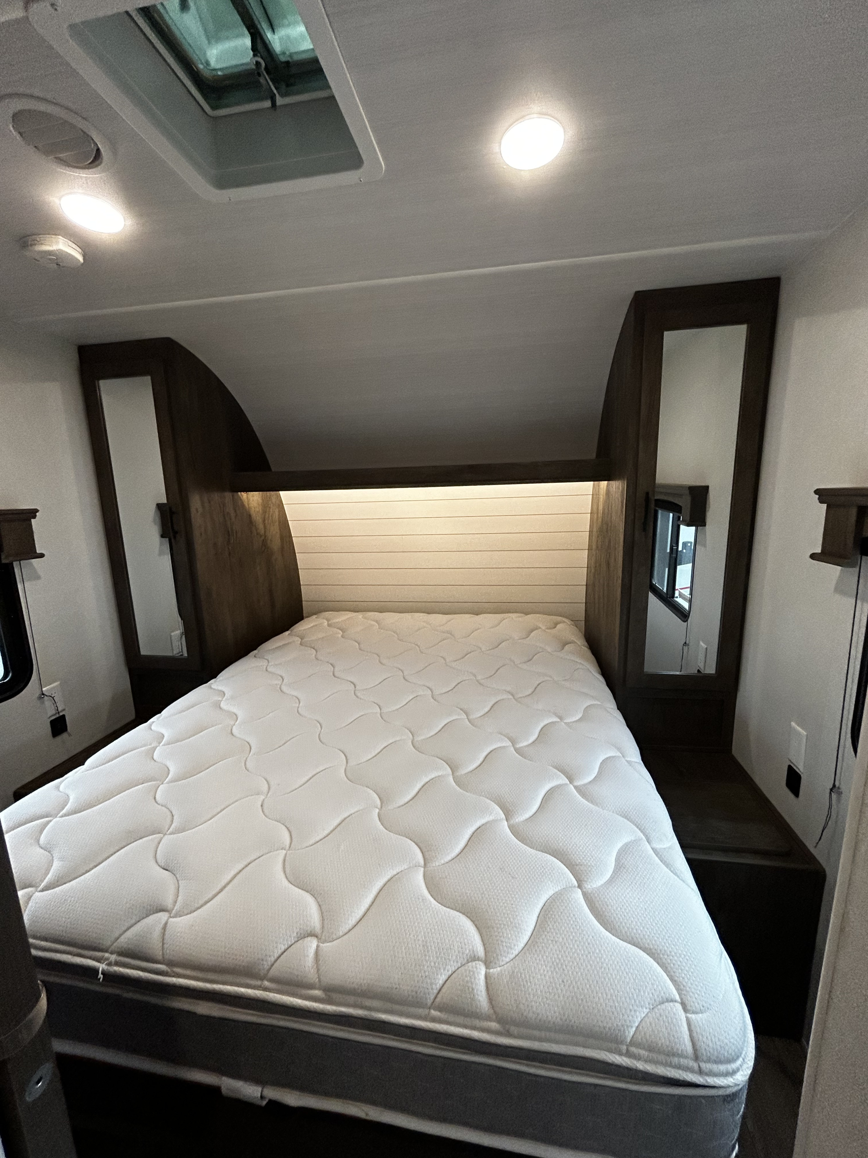 Modern RV rental bedroom with comfortable mattress, built-in headboard storage, mirrors, and ceiling lights.. Forest River Shockwave 2021