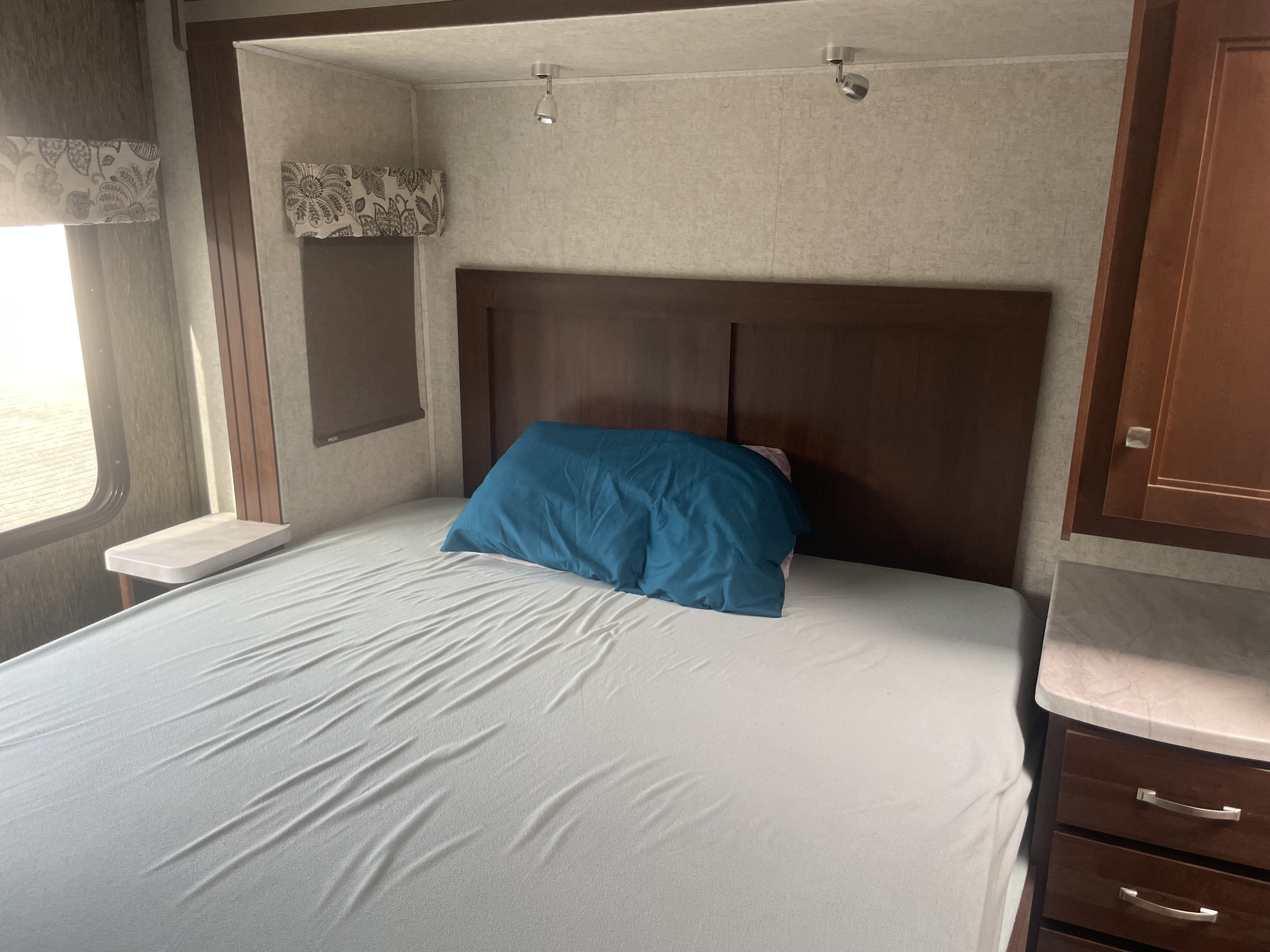 RV rental bedroom with a comfortable white bed, blue pillow, dark wood headboard, and a bright window.. Forester Forester Motorhome 2019