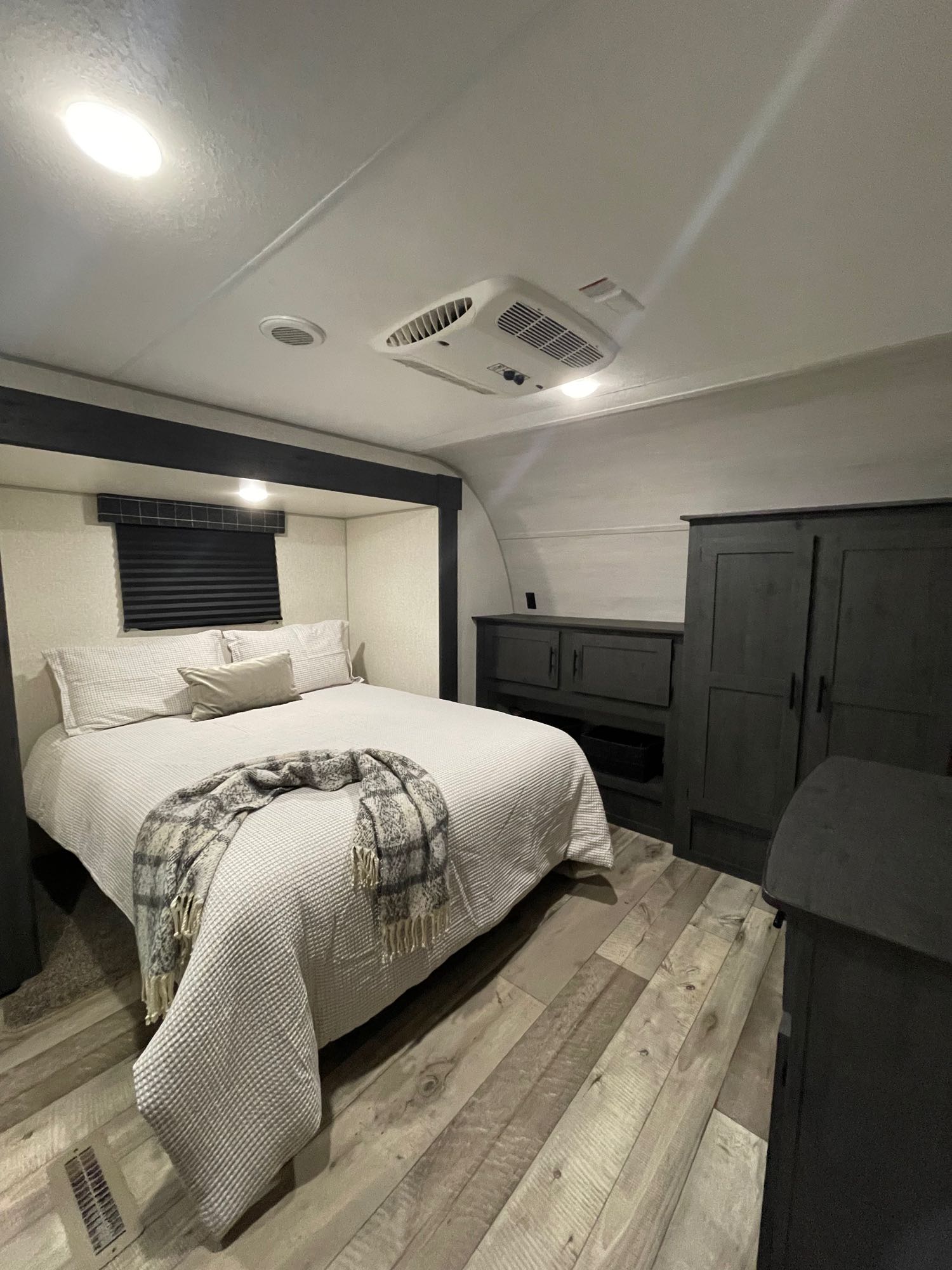 Step into this cozy RV rental bedroom. It features a comfortable bed, dark cabinets, light wood-look flooring, and an overhead AC unit.. KZ Sportsmen 2022