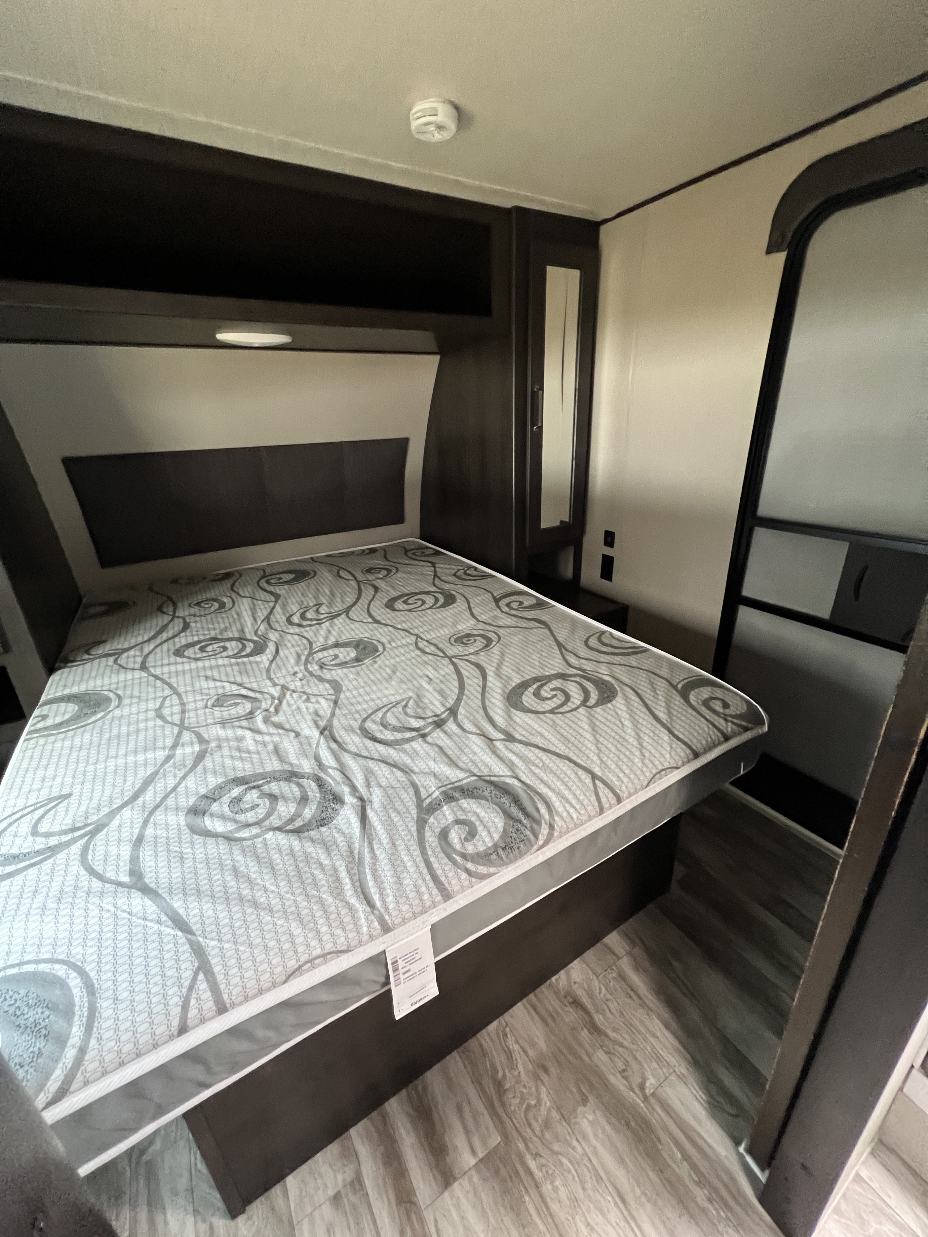 Cozy RV rental bedroom with patterned mattress, overhead storage, mirrored closet, and wood-look flooring.. Grand Design Transcend Xplor 2021