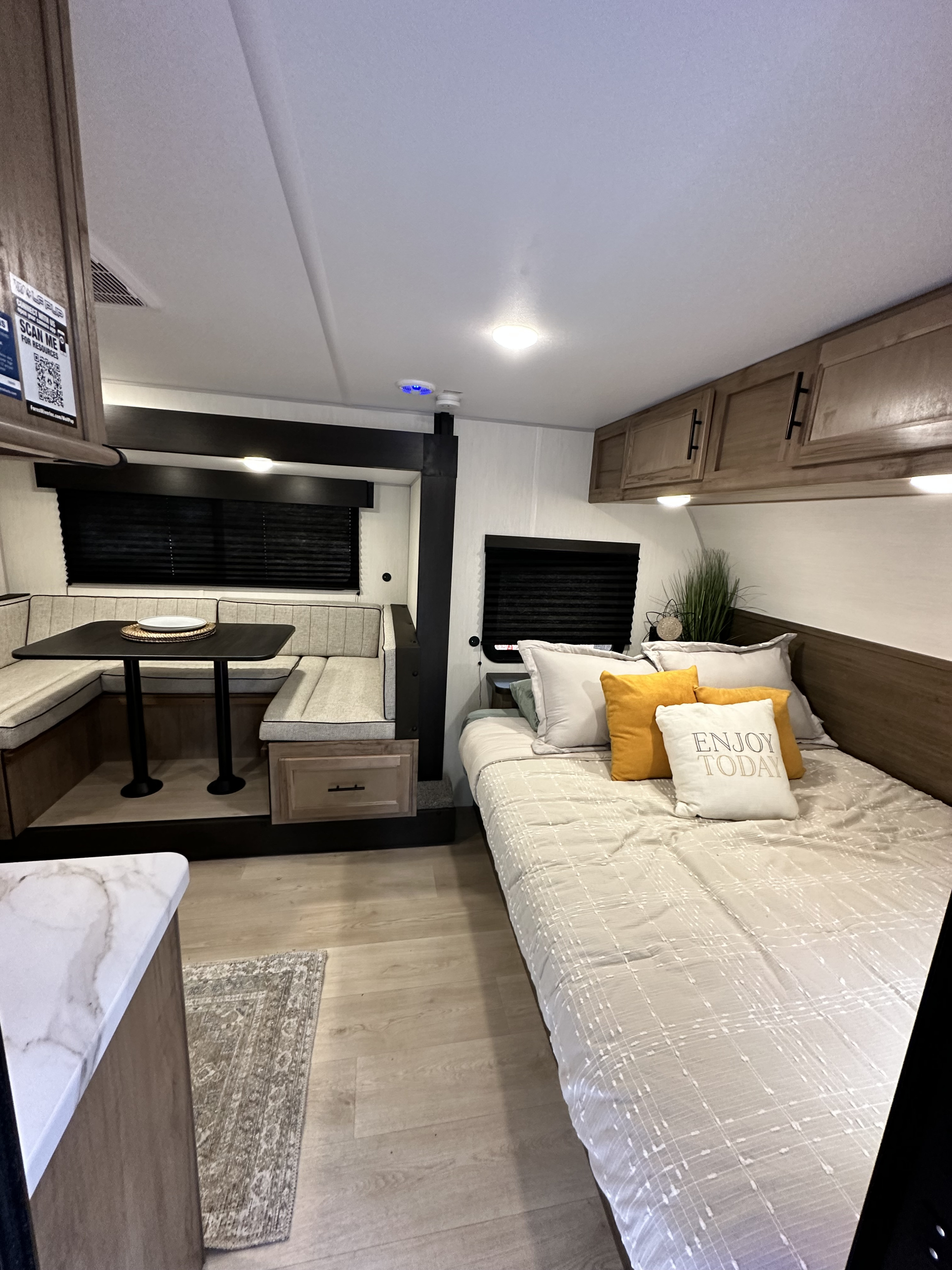This RV rental interior features a cozy dining booth, bed with "ENJOY TODAY" pillow, and overhead storage.. Cherokee Wolf pup 2025