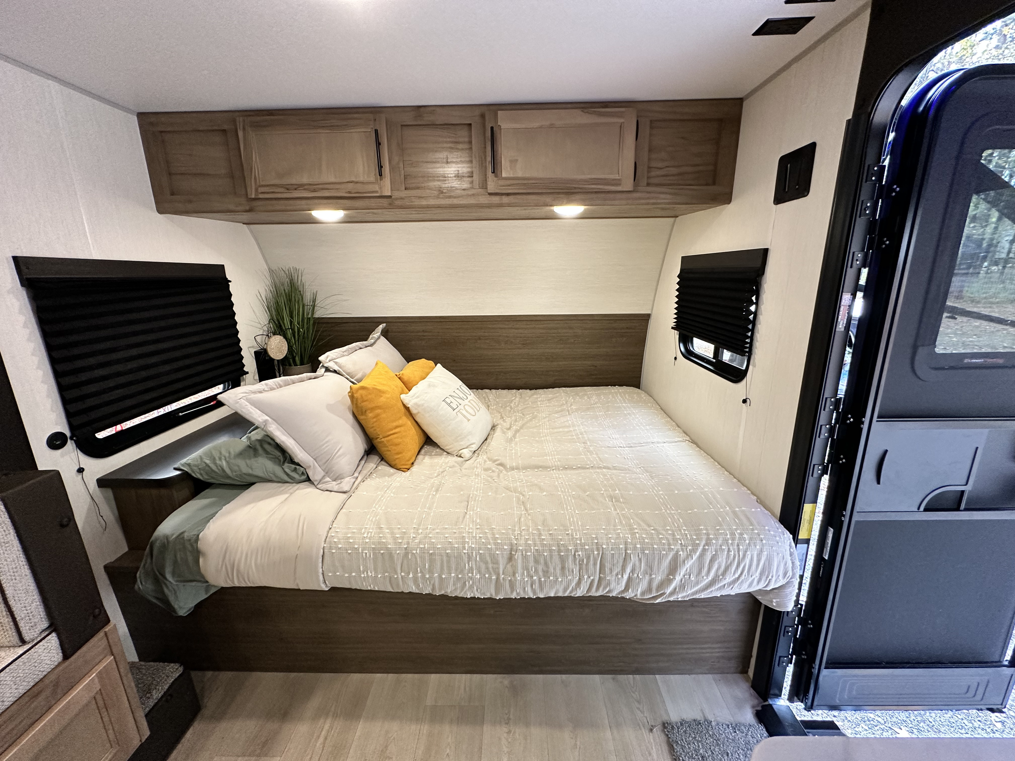 Inviting RV rental bedroom with a queen bed, decorative pillows, overhead cabinets, and side windows with blinds.. Cherokee Wolf pup 2025