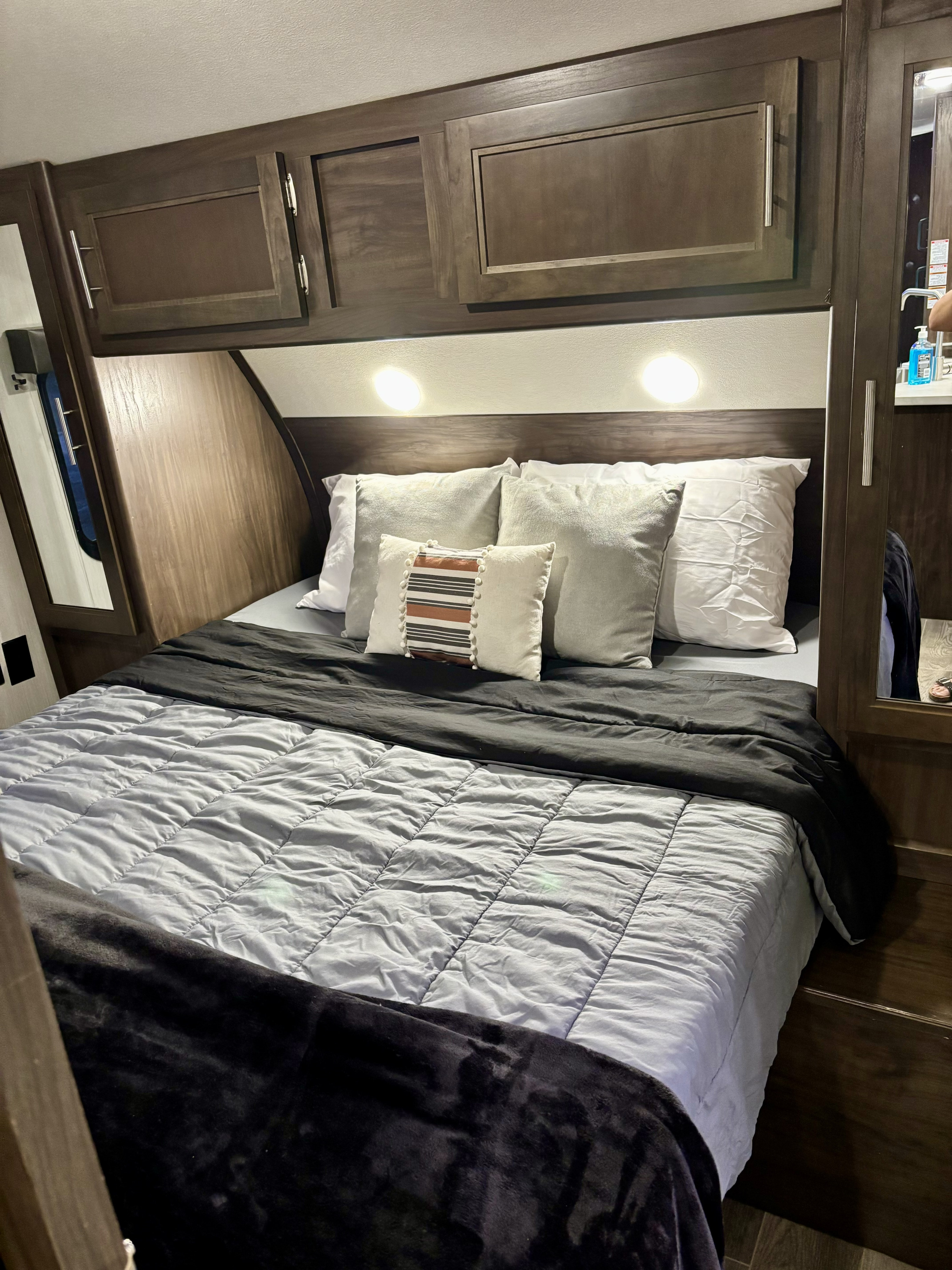 Cozy RV rental bedroom featuring dark wood overhead cabinets, bright reading lights, and comfortable bedding for travel comfort.. Forest River Cherokee Grey Wolf 2019