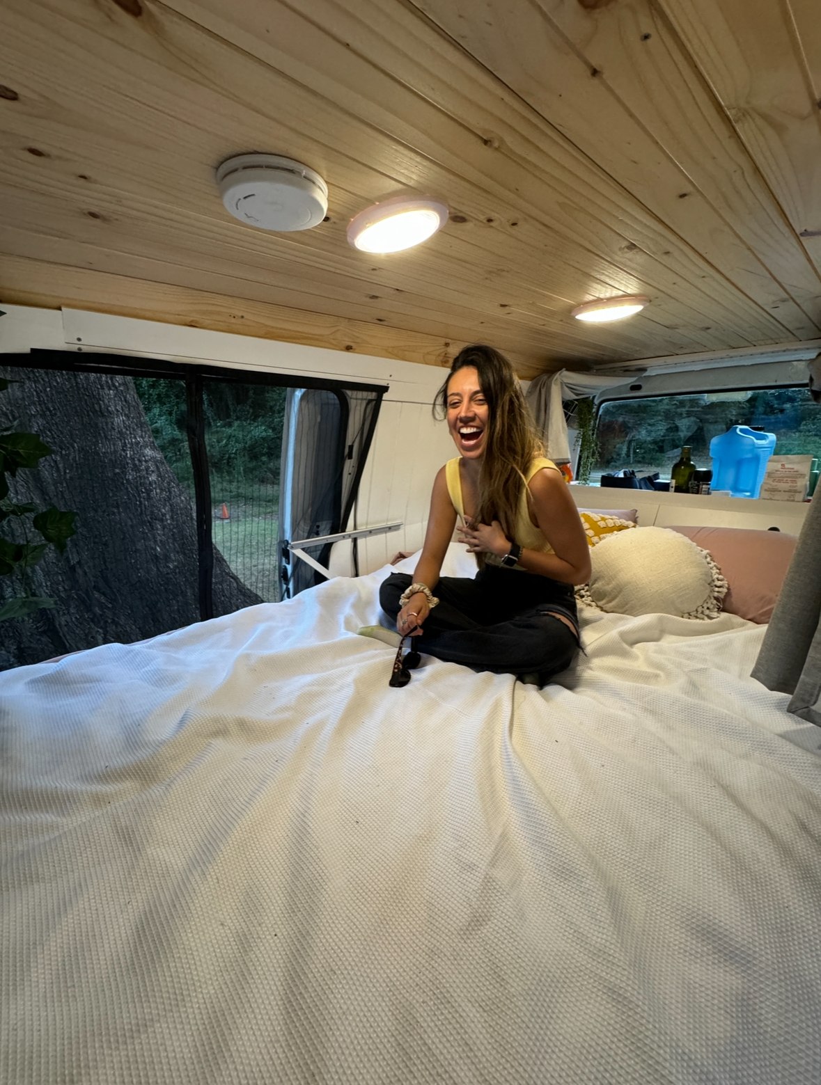 A cheerful woman with long hair sits cross-legged, laughing on a large white bed inside a cozy RV rental.. Mitsubishi Mitsubishi Express camper van w/Solar power motorhome. 2013