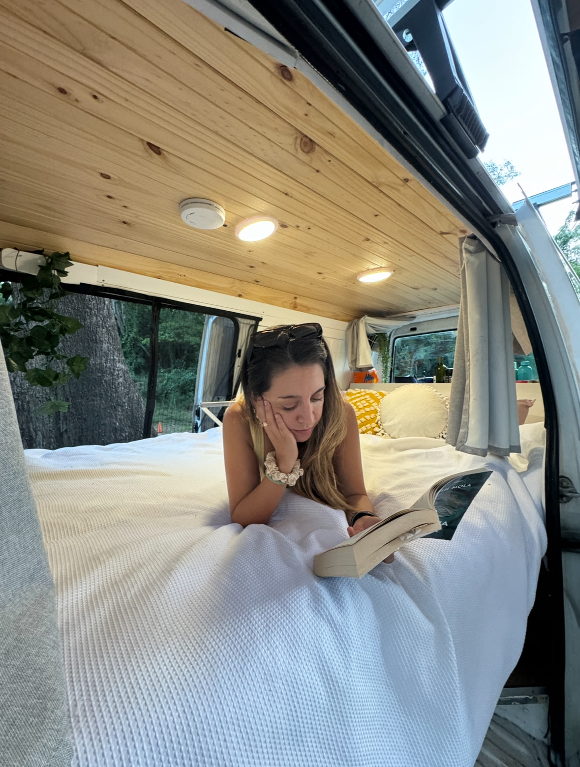Relax in your RV rental! A woman enjoys a book on the comfy bed of her converted travel van, surrounded by nature.. Mitsubishi Mitsubishi Express camper van w/Solar power motorhome. 2013