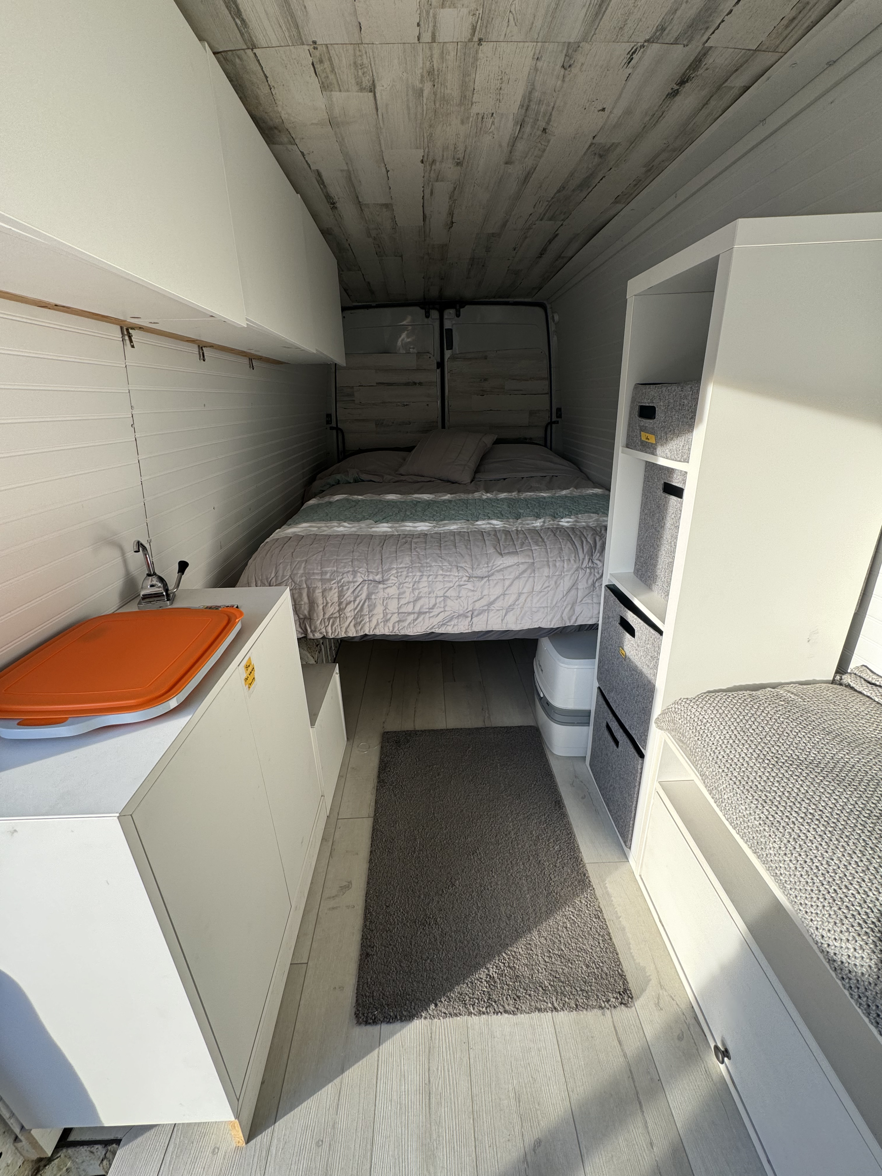 Modern RV rental interior with a comfy bed, compact kitchen setup, and organized storage units, ideal for mobile living.. Dodge Sprinter Van 2005