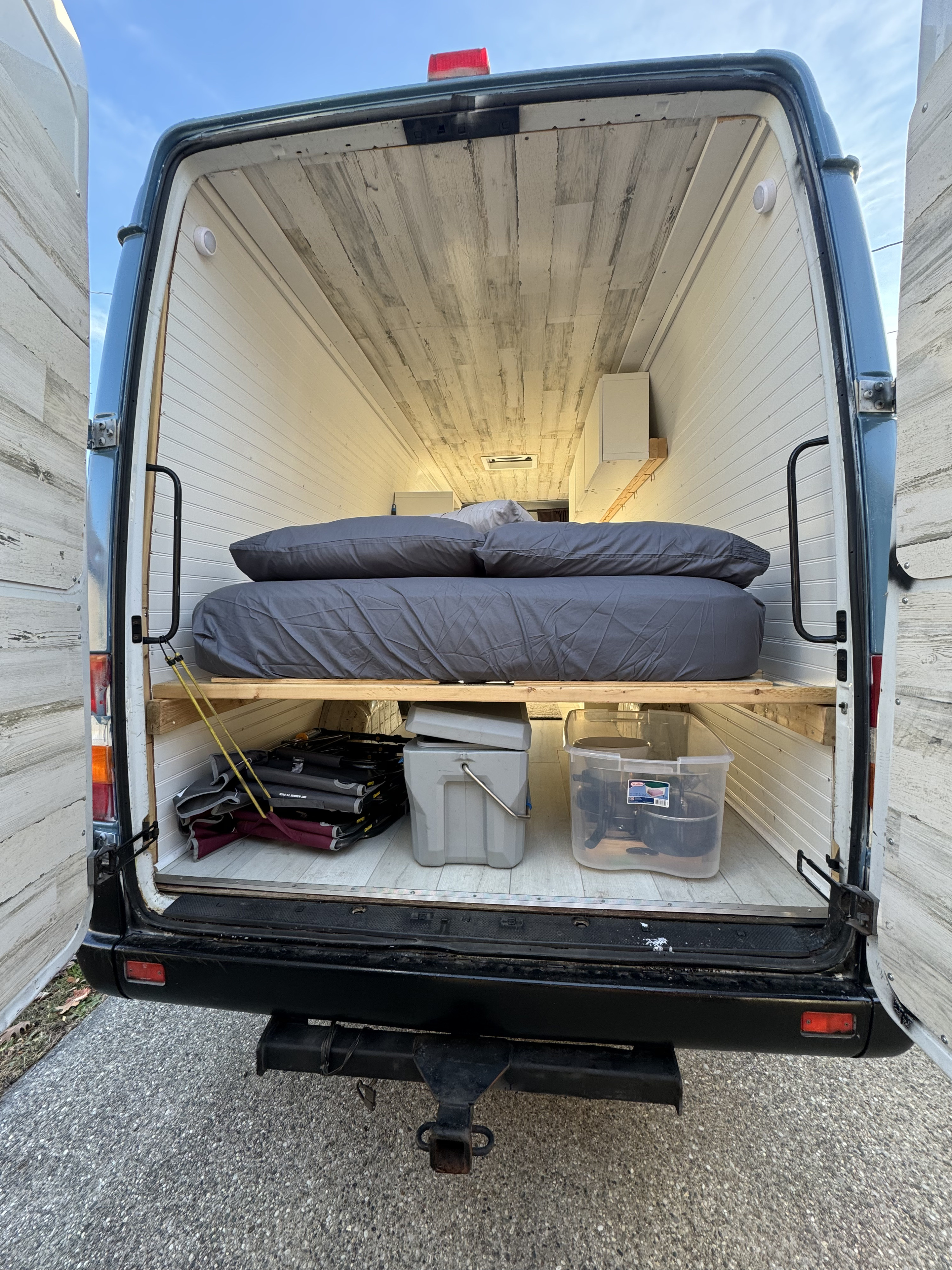 This RV rental's camper van interior features a raised bed, under-bed storage, and light wood-look paneling.. Dodge Sprinter Van 2005