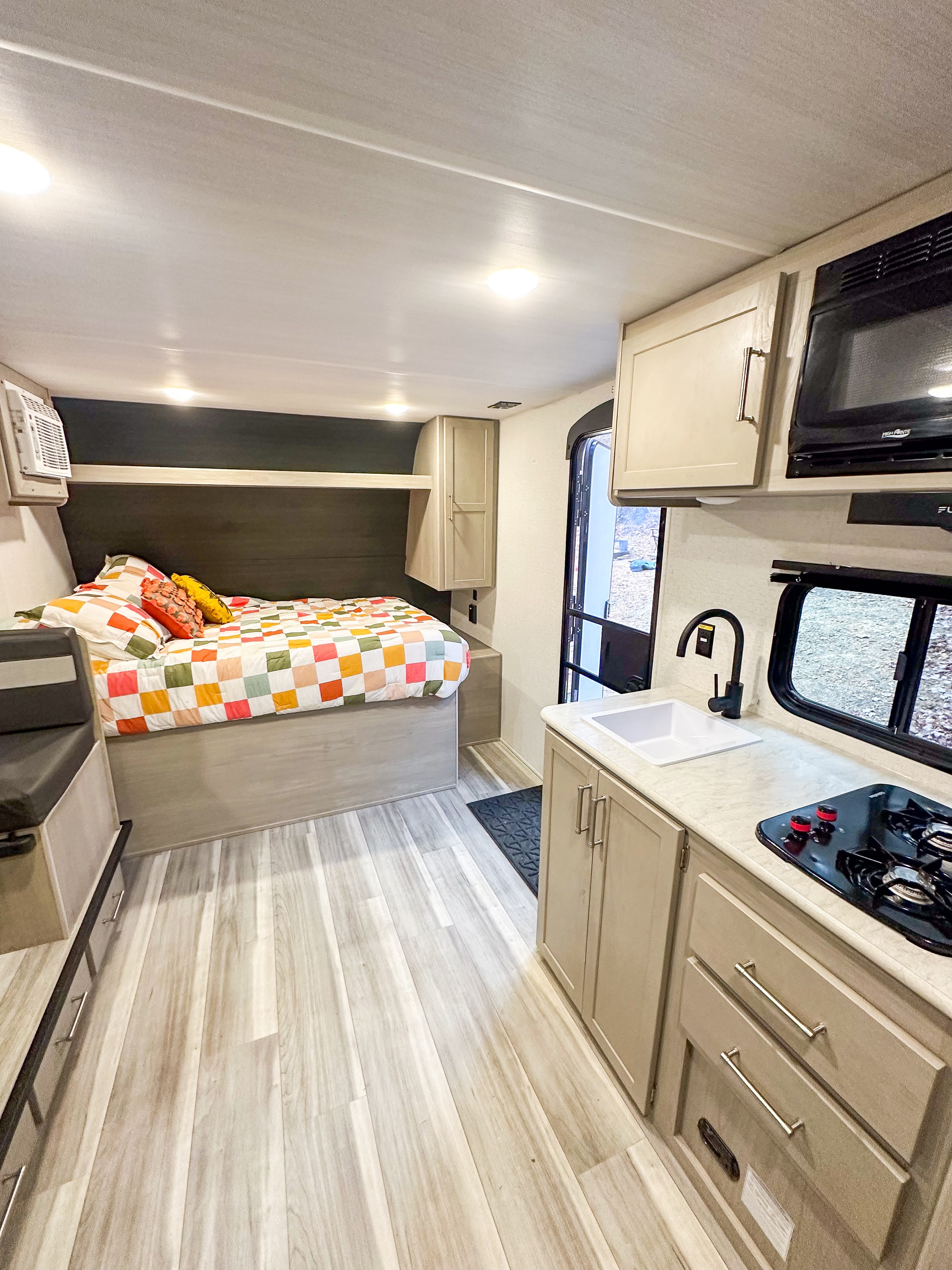 Explore this modern RV rental interior featuring a comfy bed with a colorful quilt, a compact kitchen, and light wood floors.. Keystone RV Springdale 2024