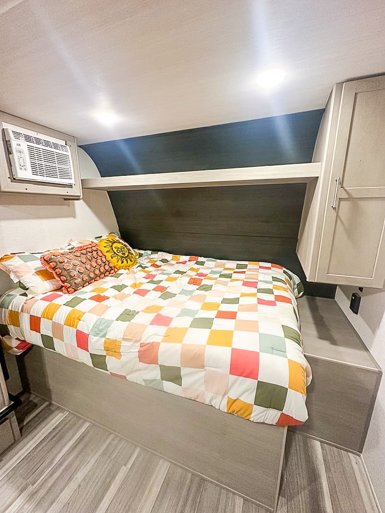 This RV rental offers a cozy bedroom with a colorful quilt, built-in AC unit, and overhead storage.. Keystone RV Springdale 2024