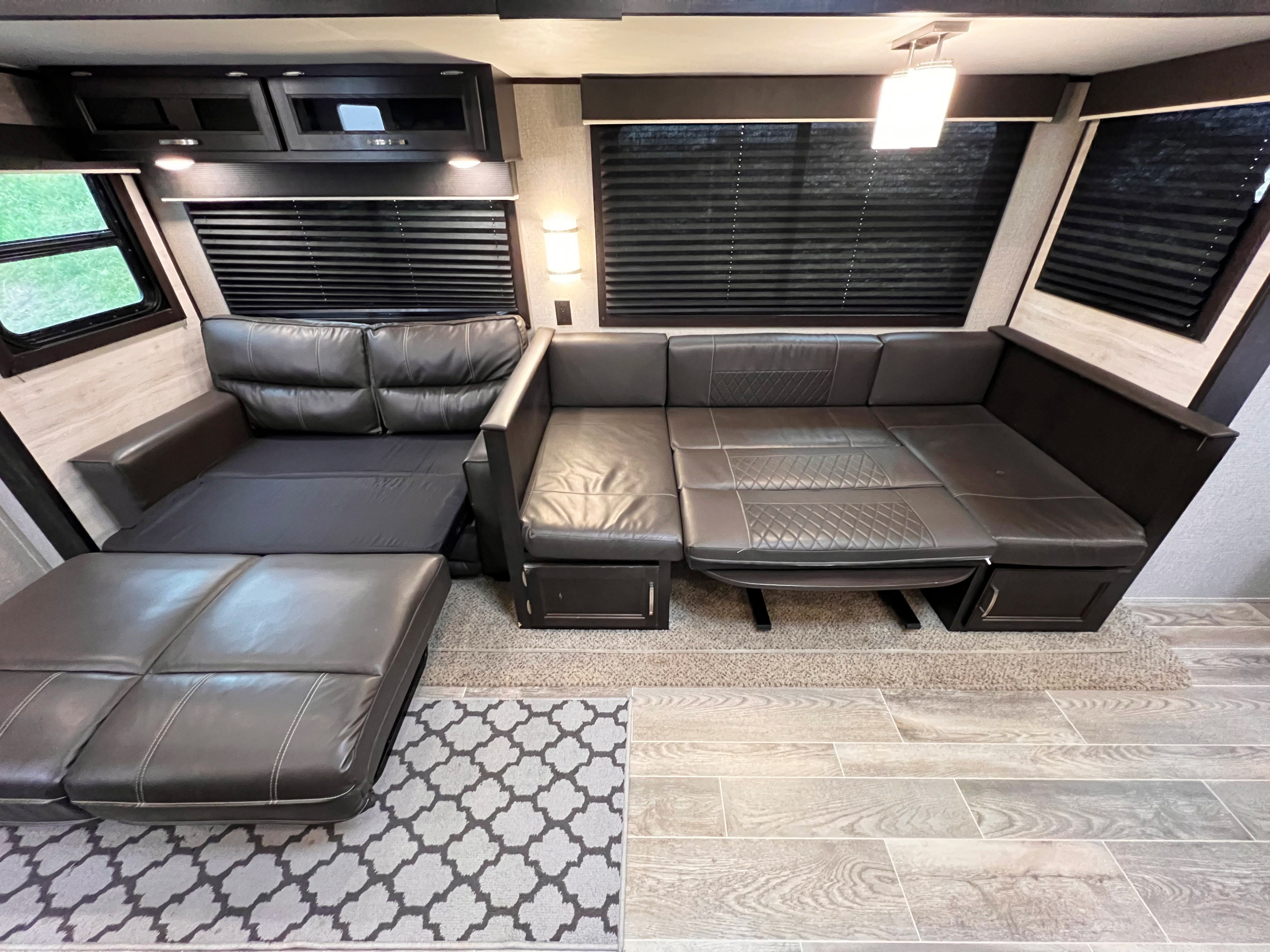 Interior of an RV rental: a versatile living space with a large sofa converting to a bed, overhead cabinets, and blinds.. Jayco Jayflight 2021