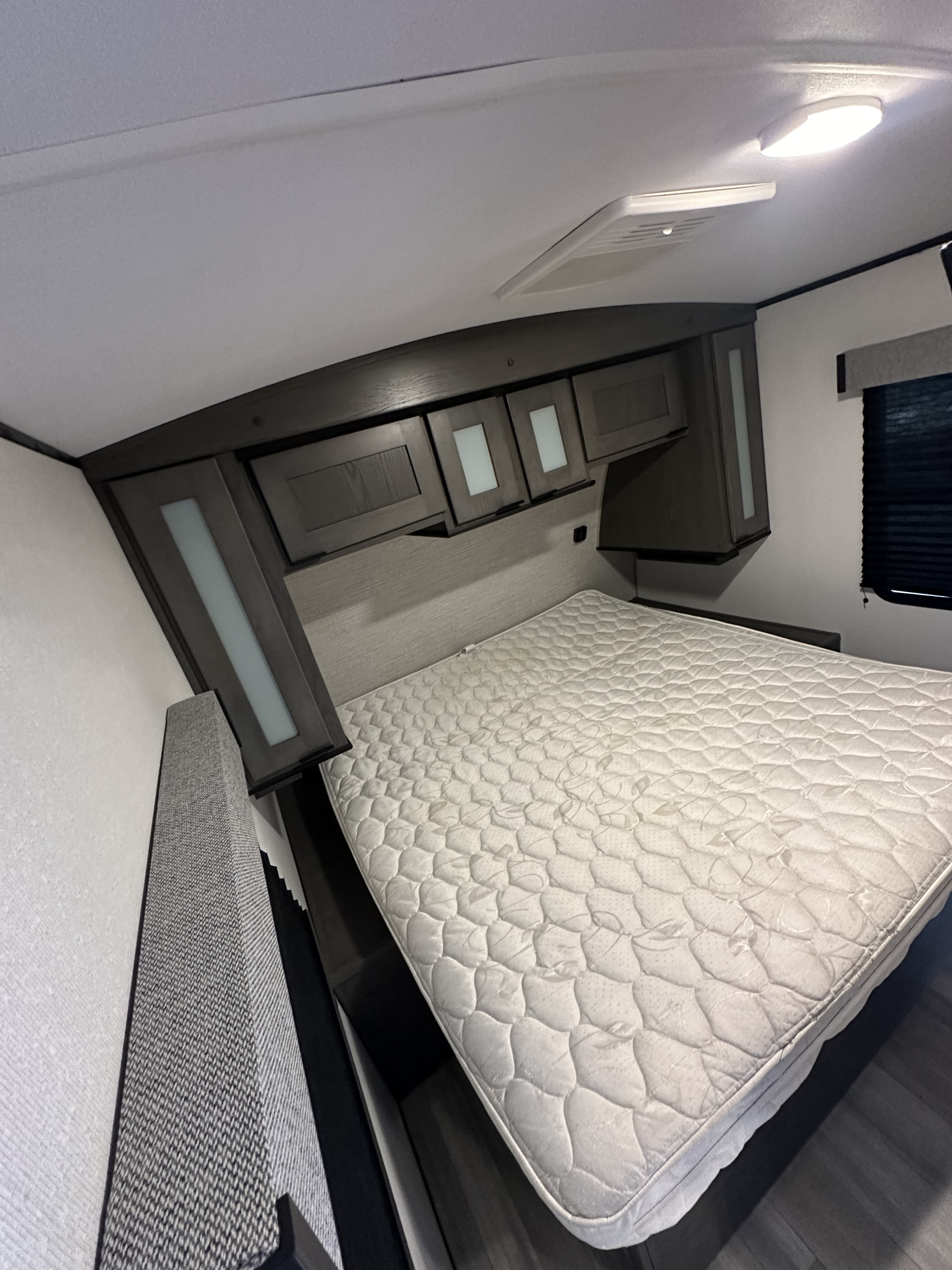 Compact RV rental bedroom with a white mattress, overhead storage, and window, providing a cozy sleeping space.. Heartland RVs MPG 2800QB 2021