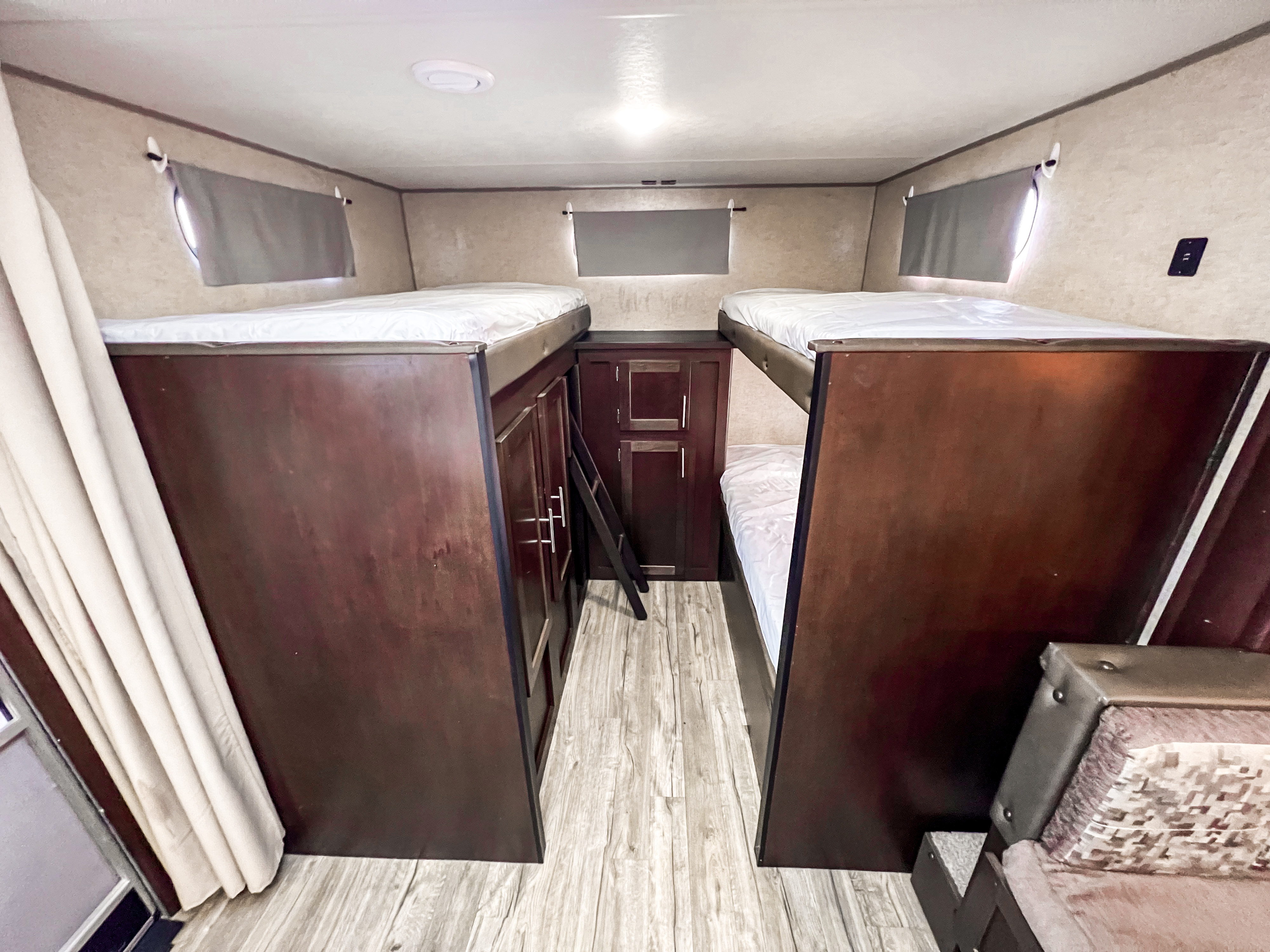 This RV rental features a compact bunk bed room with dark wood storage and a ladder, offering four sleeping berths.. Forest River Grey Wolf 2019