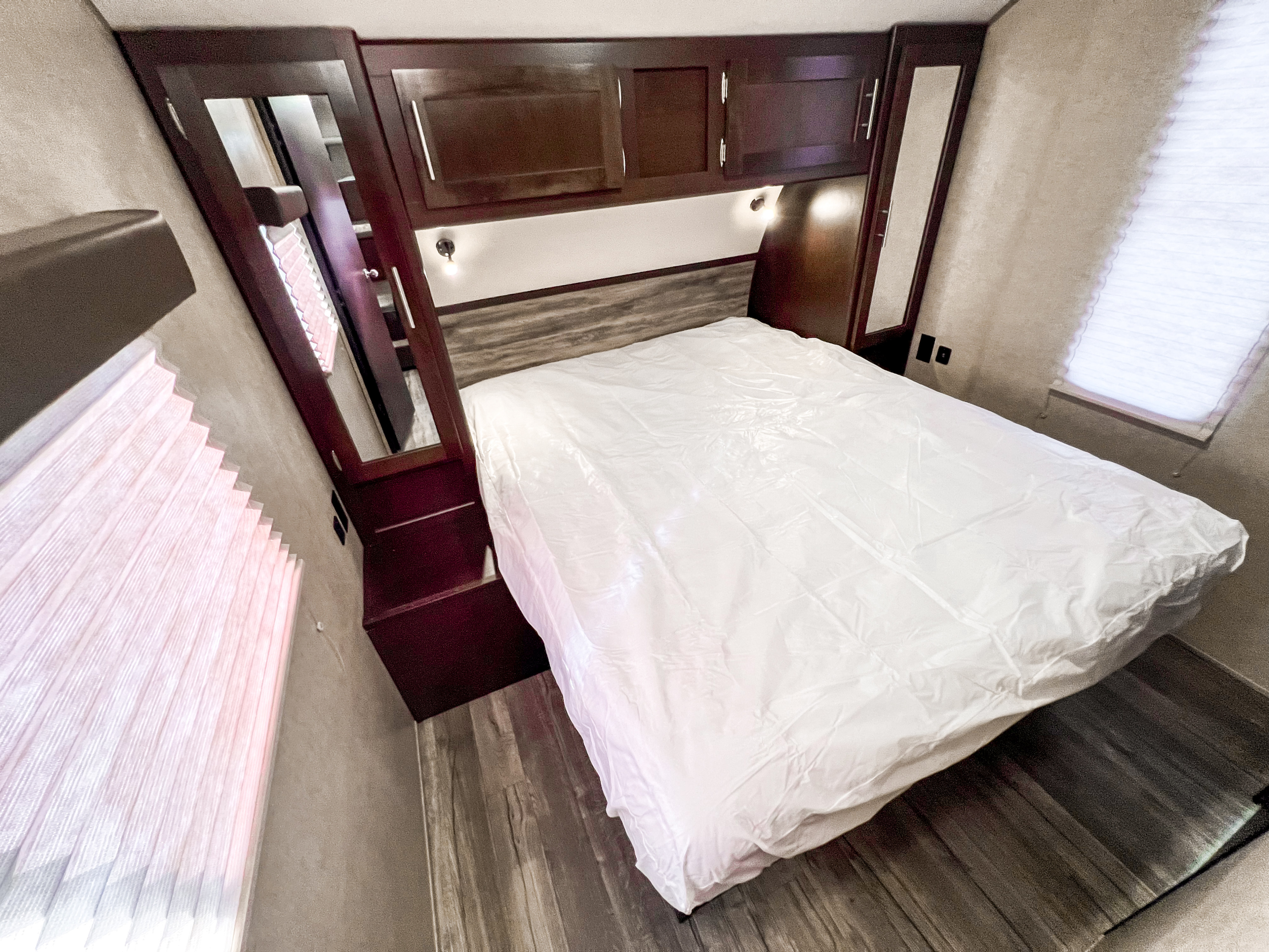 Cozy RV rental bedroom with a fresh, plastic-covered bed, dark wood cabinets, and large windows with blinds.. Forest River Grey Wolf 2019