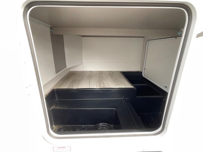 Inside an RV rental: a large storage compartment with a raised, wood-look platform and tiered black bins.. Coachmen Freelander 2025