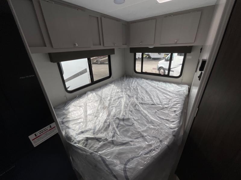 Compact RV rental bedroom, featuring a new, plastic-covered bed, overhead cabinets, and two windows for scenic views.. Coachmen Freelander 2025