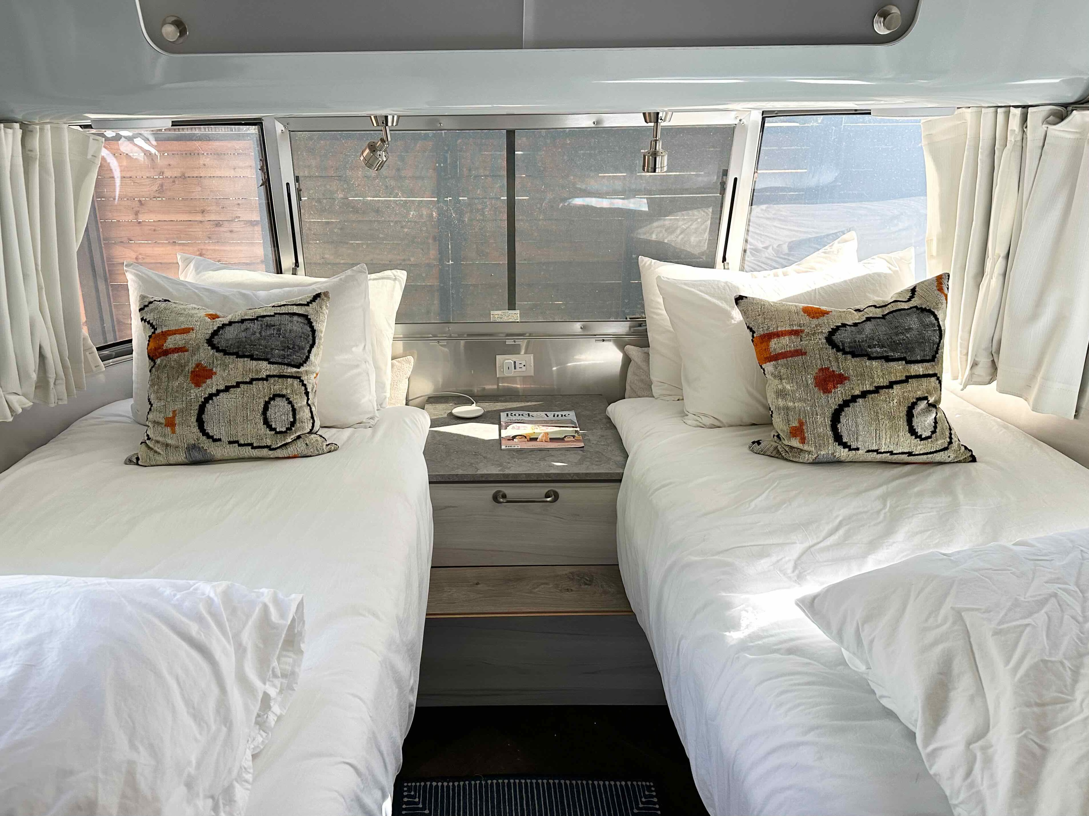 Stylish Airstream RV rental bedroom: two twin beds with white linens, central nightstand, and bright windows for a comfy stay.. Airstream International 2022