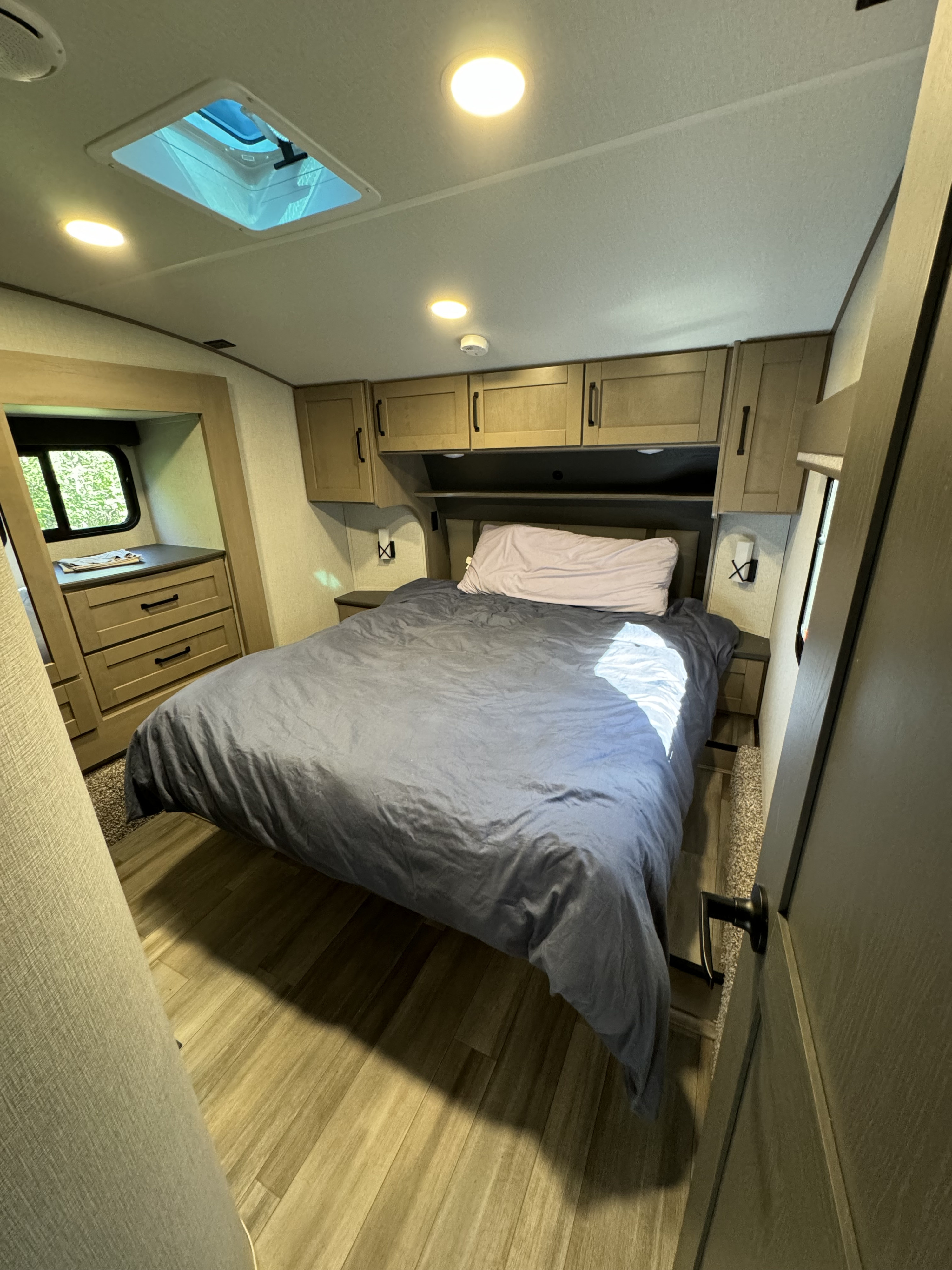 Cozy RV rental bedroom featuring a large bed, built-in dresser, ample storage cabinets, and a ceiling skylight.. Grand Design Reflection 2024