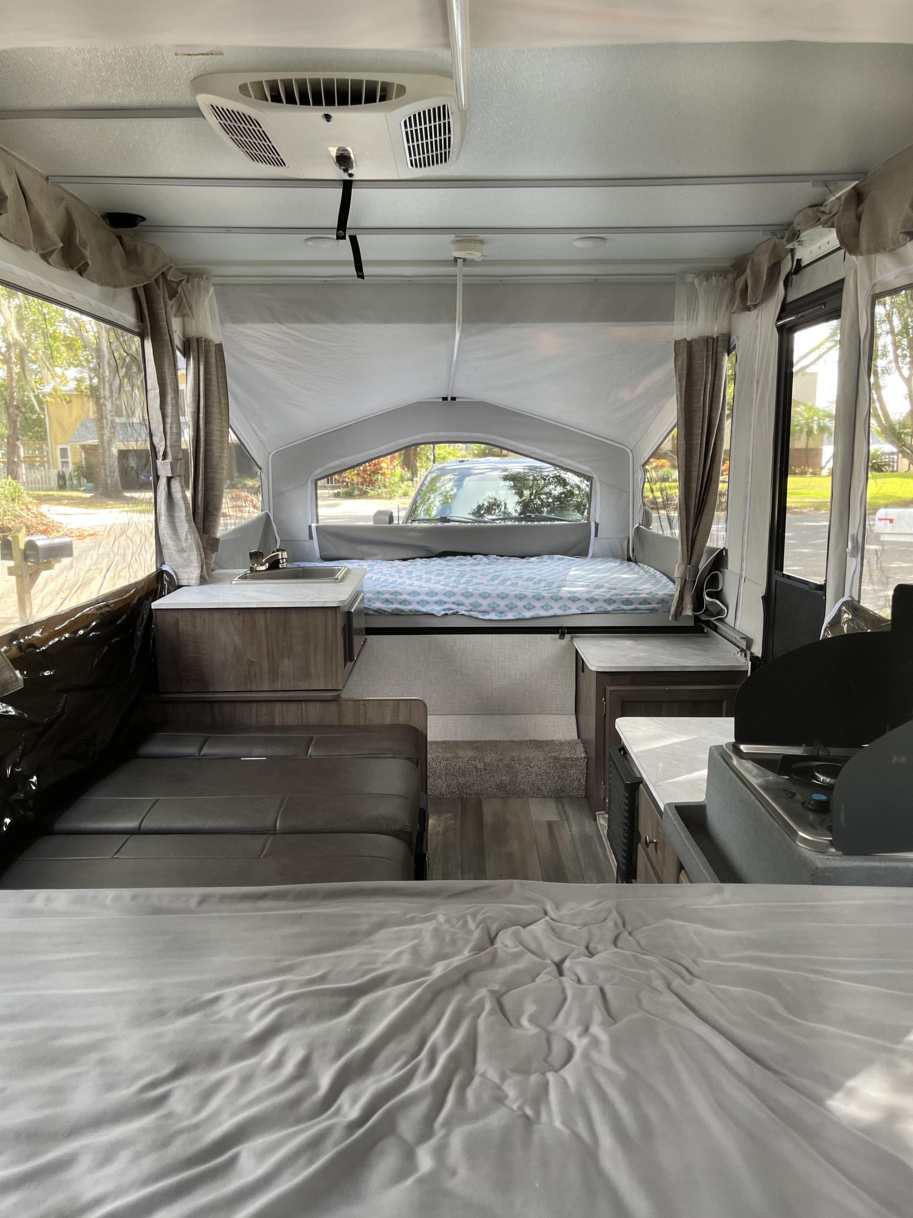 Interior view of an RV rental pop-up camper, featuring beds, a compact kitchen, and a seating area.. Forest River Flagstaff LTD 2023