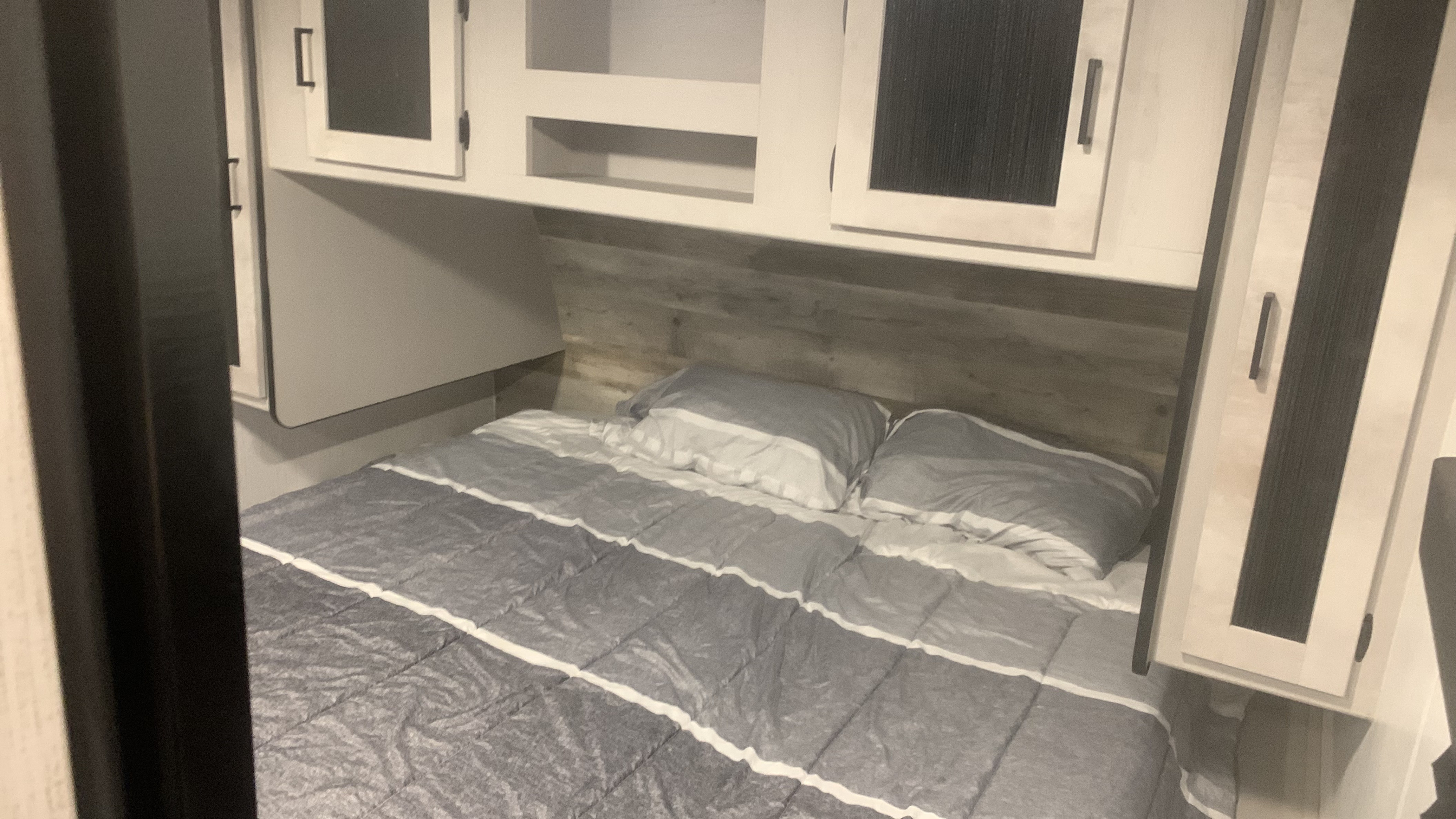 RV rental bedroom showcasing a comfortable bed with striped bedding and ample overhead cabinets.. Heartland m 2022